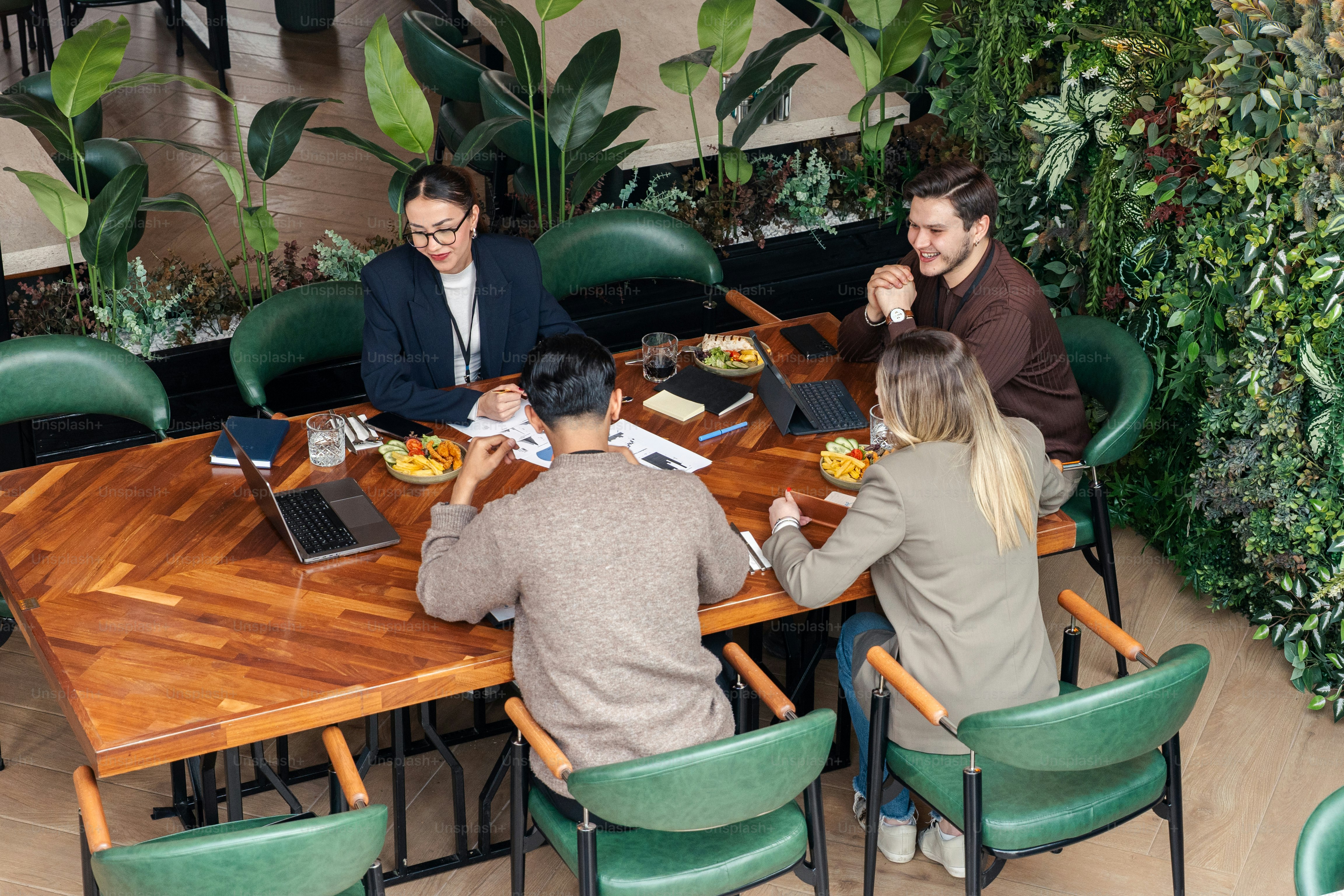 Four people collaborating around a table with plants. photo – Meeting ...