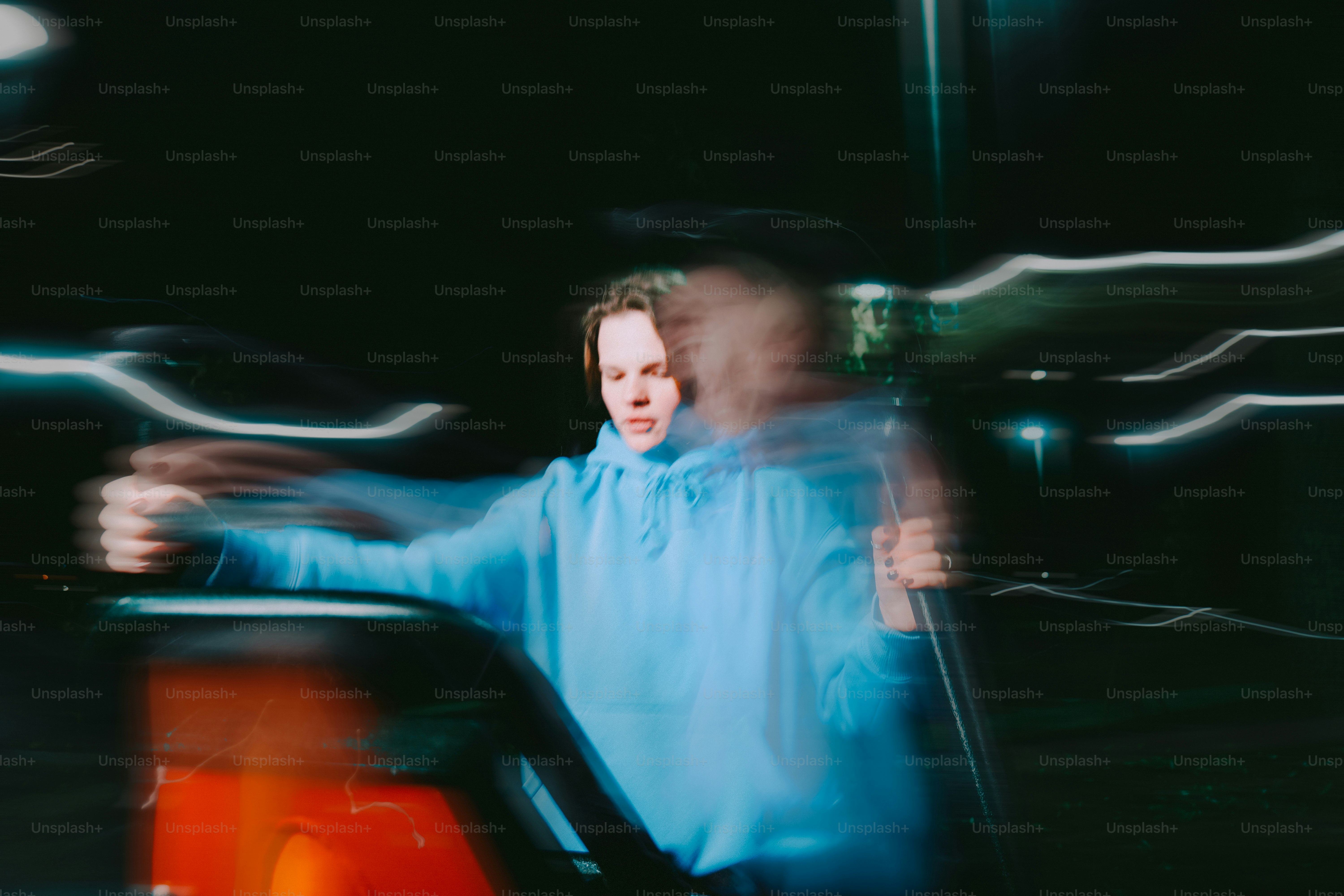 Man in blue hoodie leaning on car at night