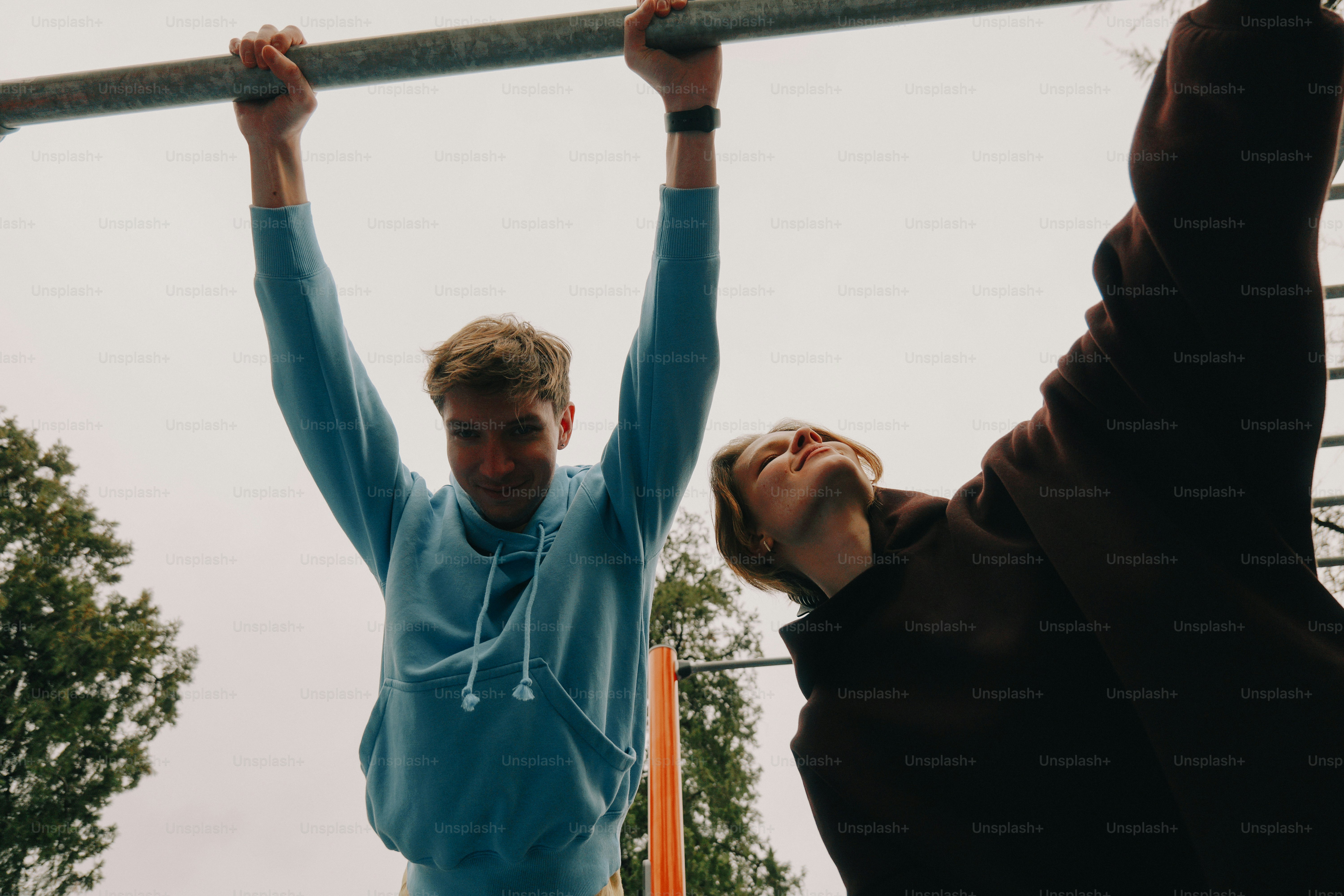 Two young men hanging from a bar outdoors