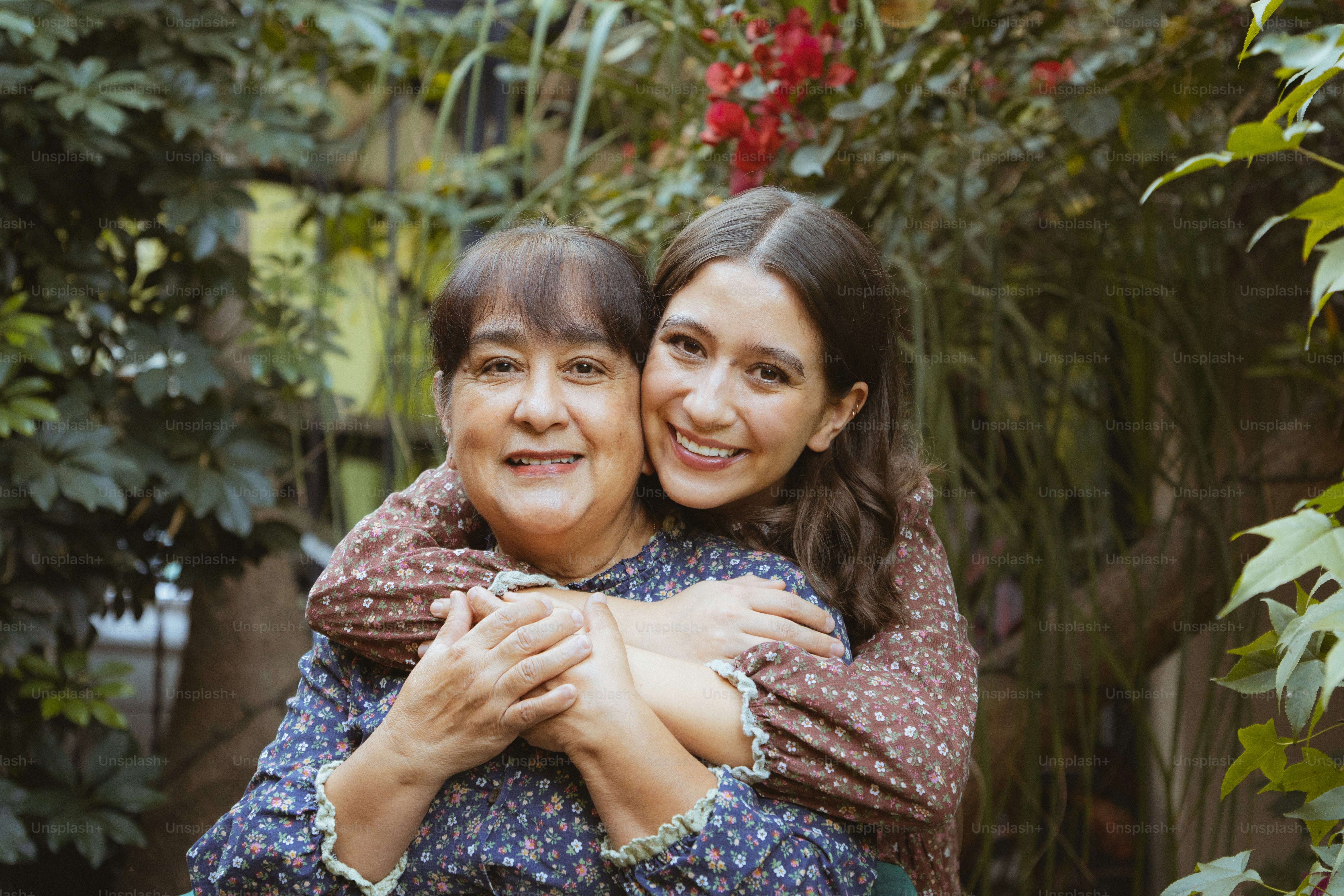 Zwei Frauen, die sich draußen umarmen, mit Laub im Hintergrund.