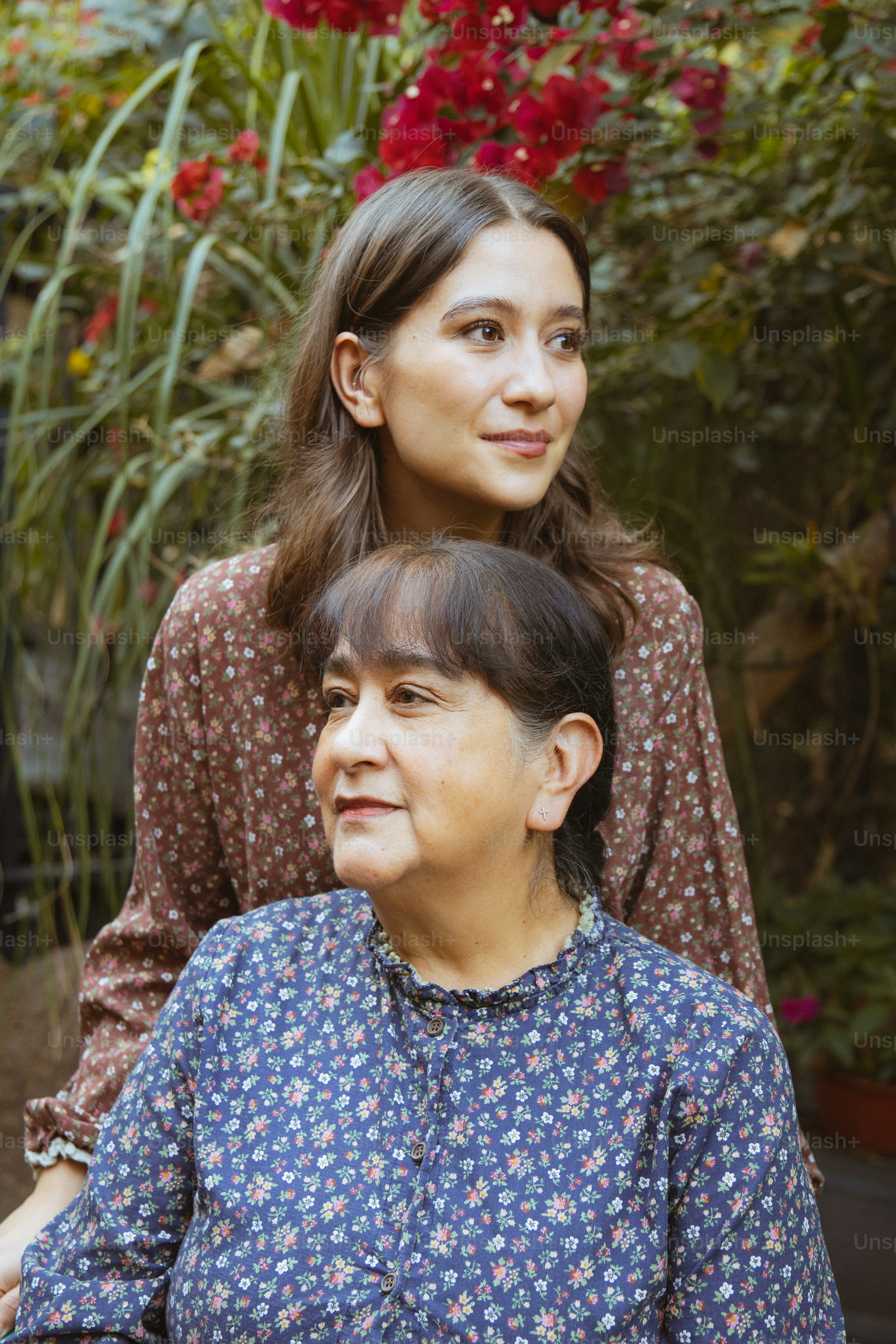 Zwei Frauen in floralen Oberteilen mit Pflanzen dahinter.
