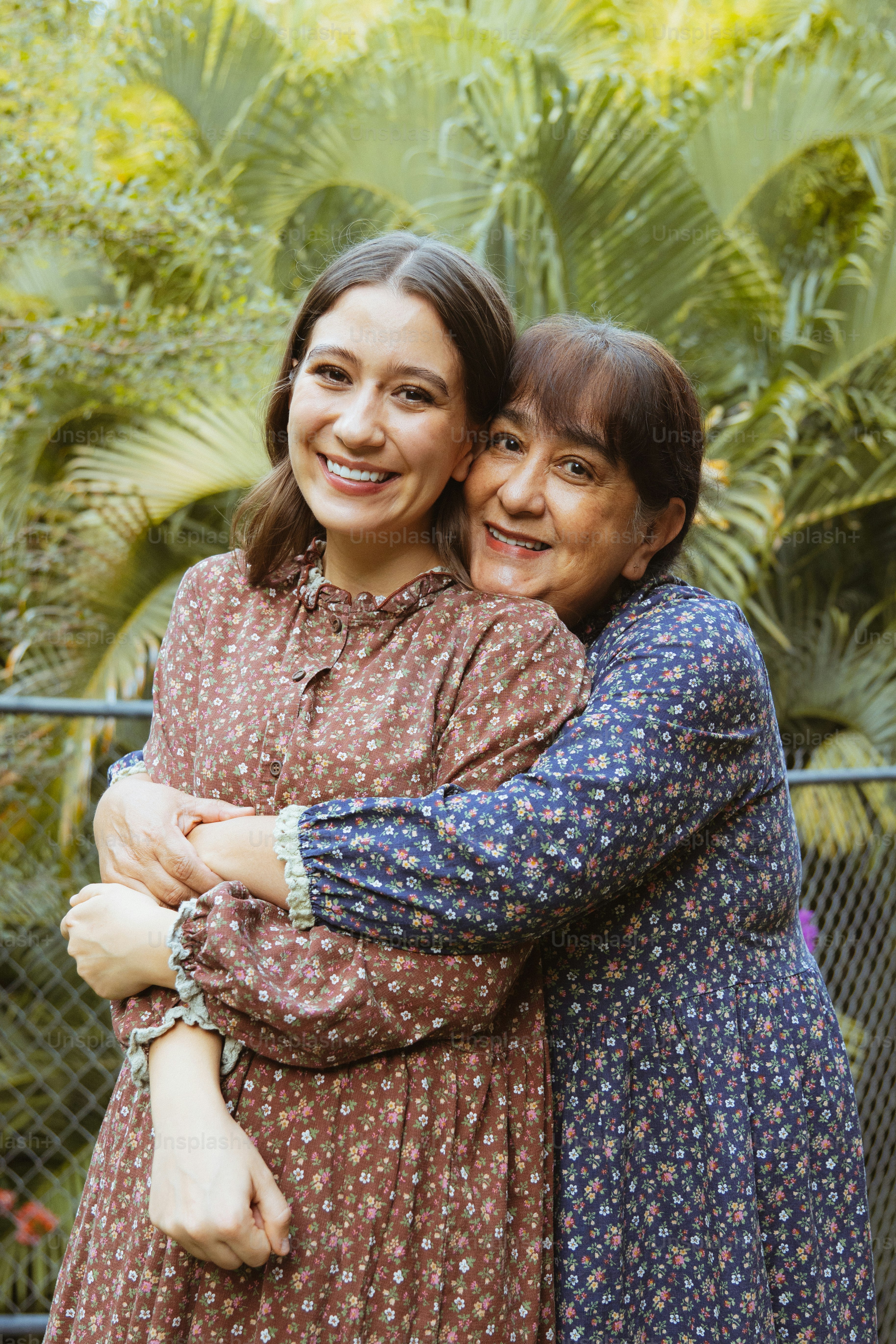 Zwei Frauen, die sich draußen umarmen, mit üppigem Grün hinter sich.