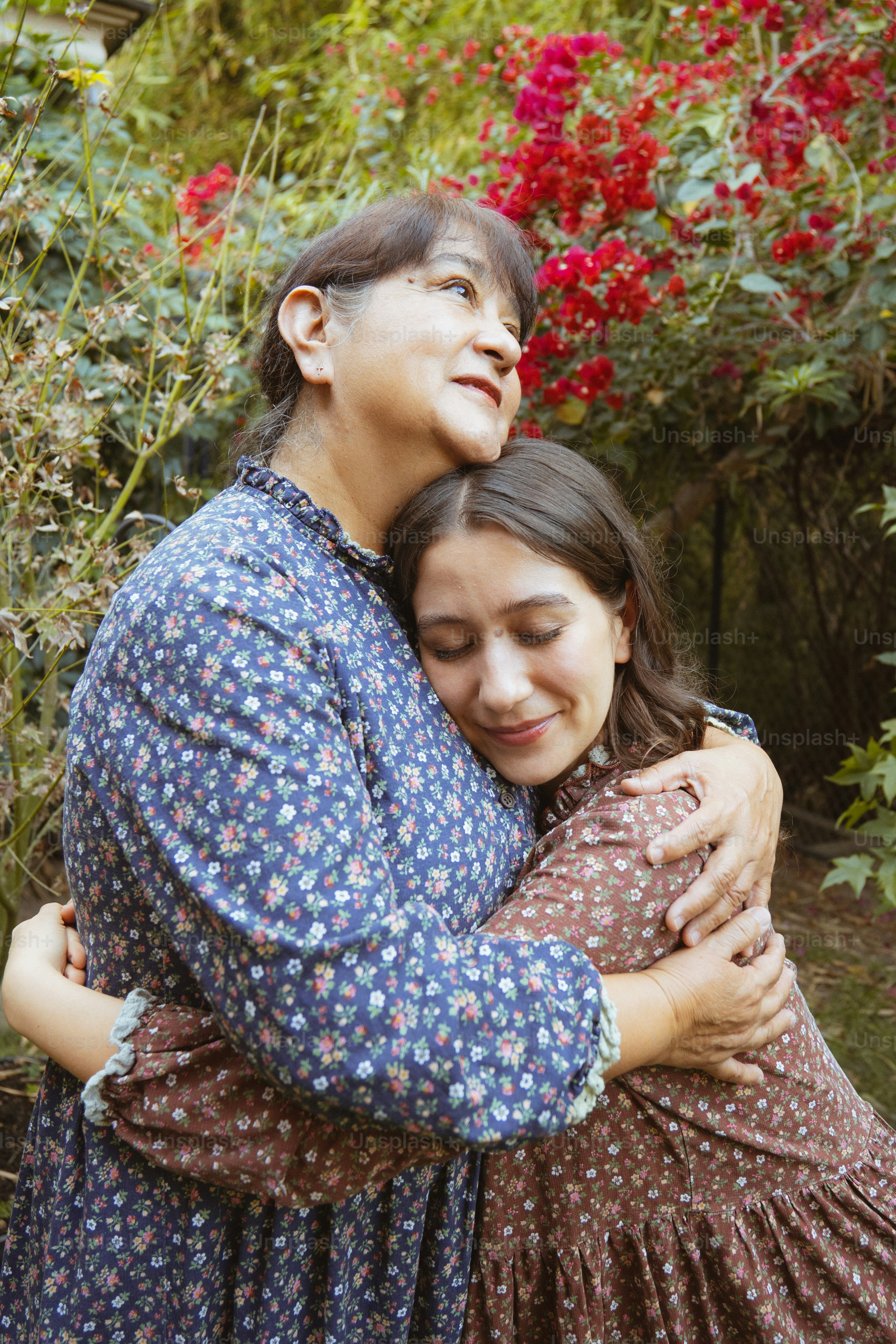 Zwei Frauen, die sich in einem Garten mit roten Blumen umarmen.