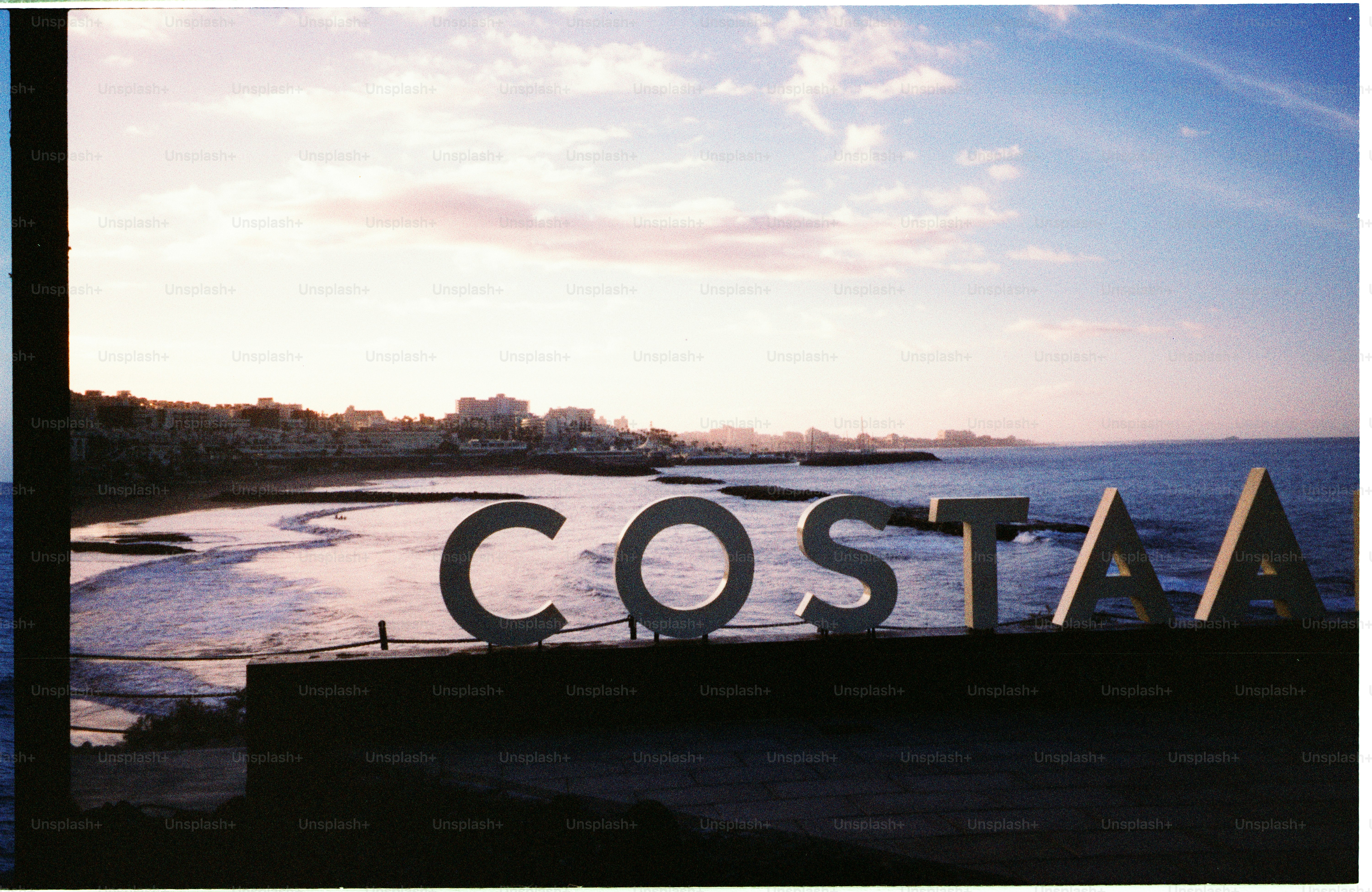 Large "costa" sign on a beach with ocean background