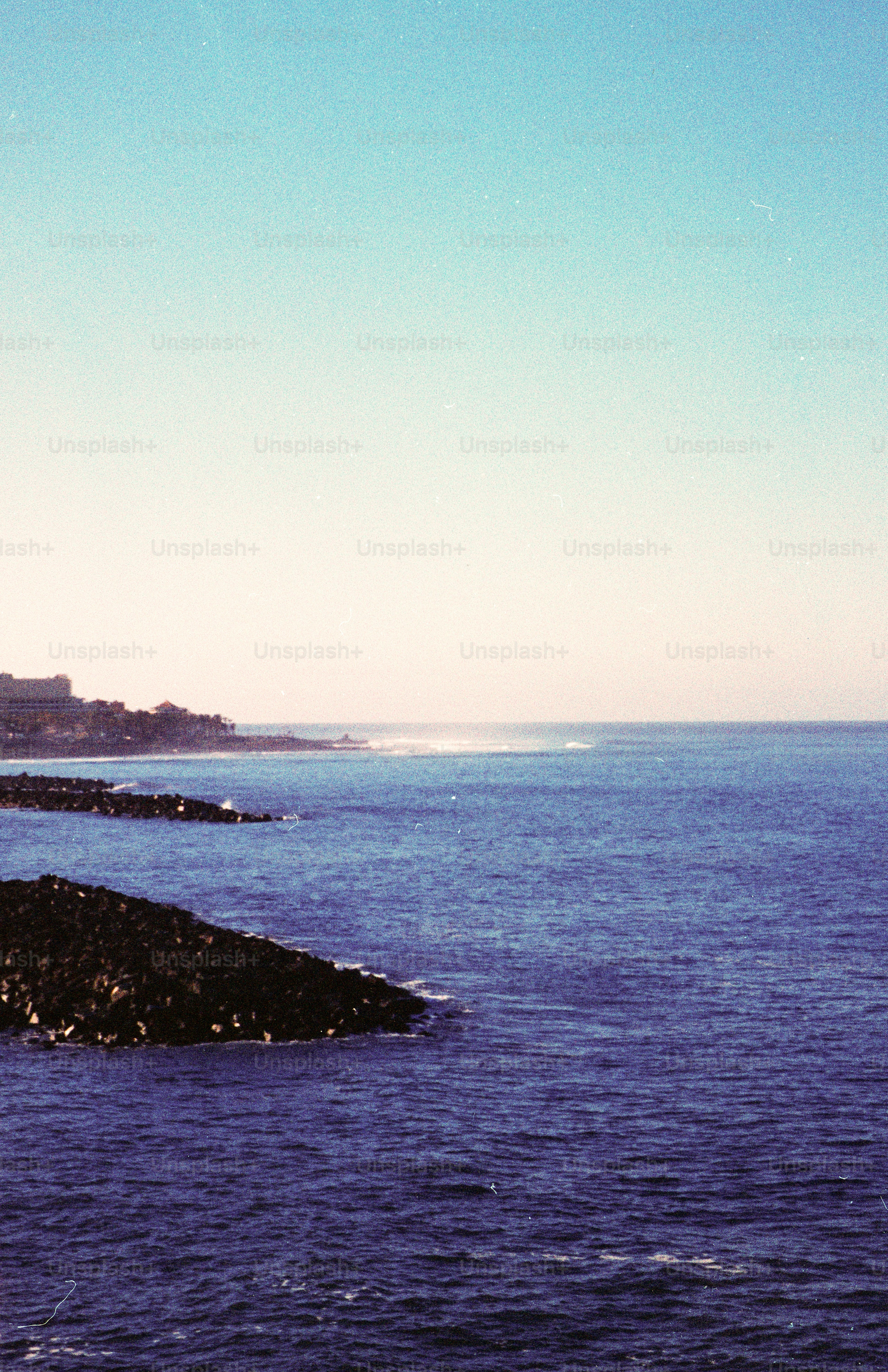 Le onde dell'oceano si infrangono contro la costa rocciosa con una città lontana.