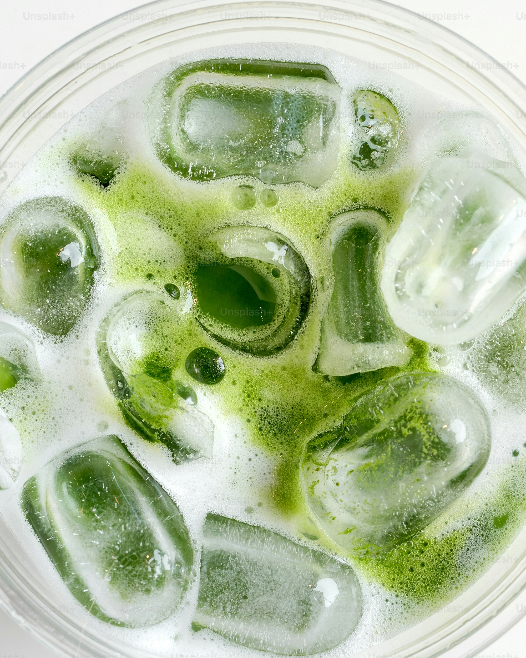 Close-up of iced matcha latte with foam and ice.