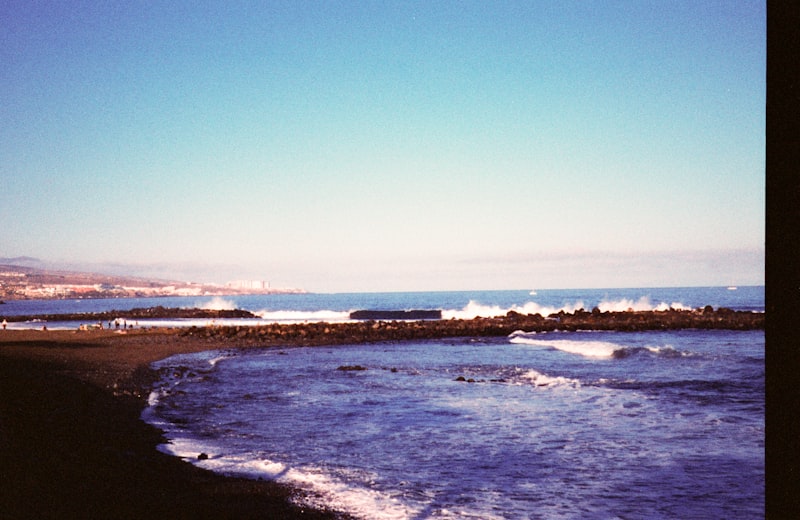Las olas rompen contra una costa rocosa bajo un cielo despejado.