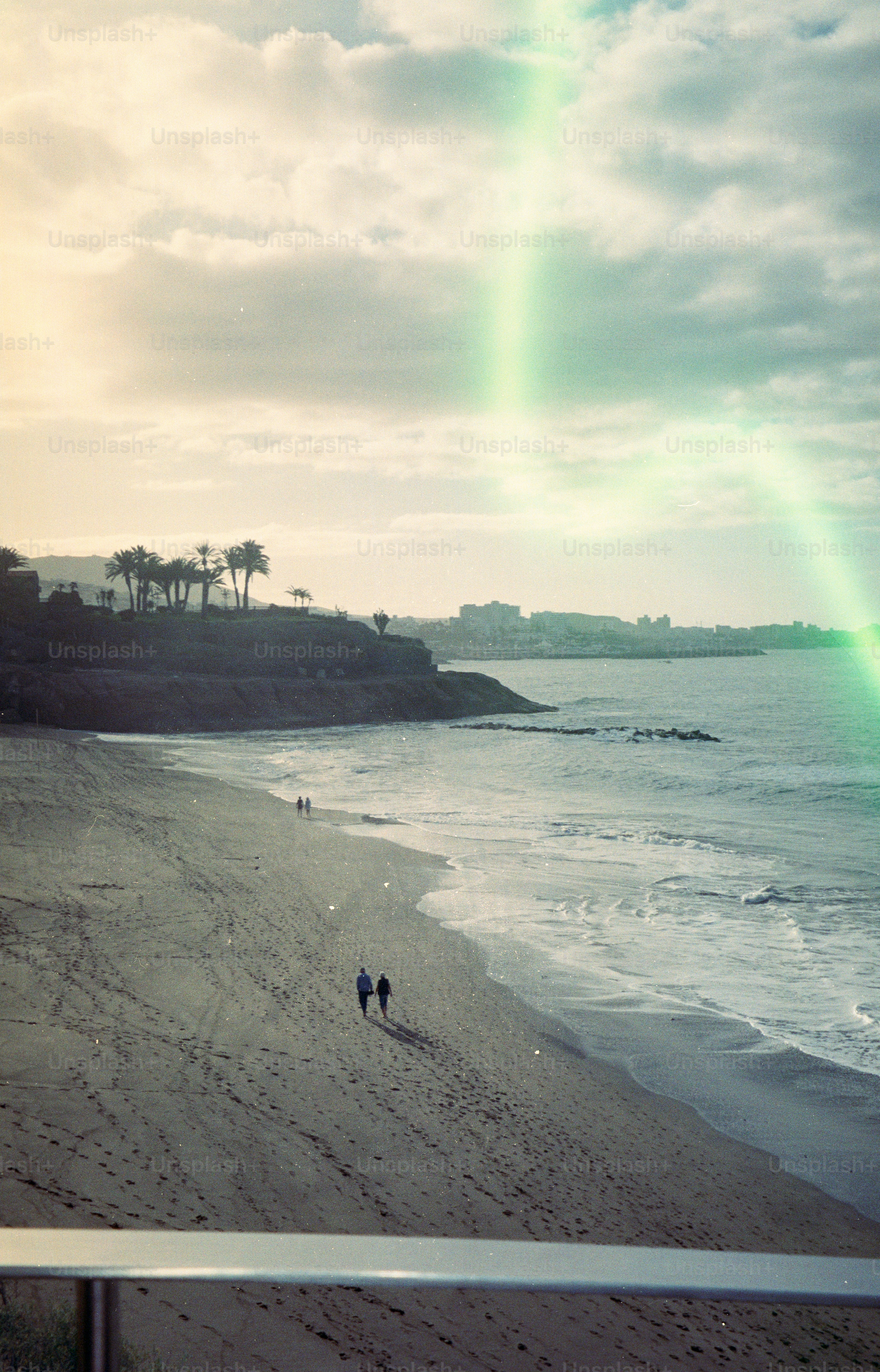 Two people walk on a sandy beach near the ocean.