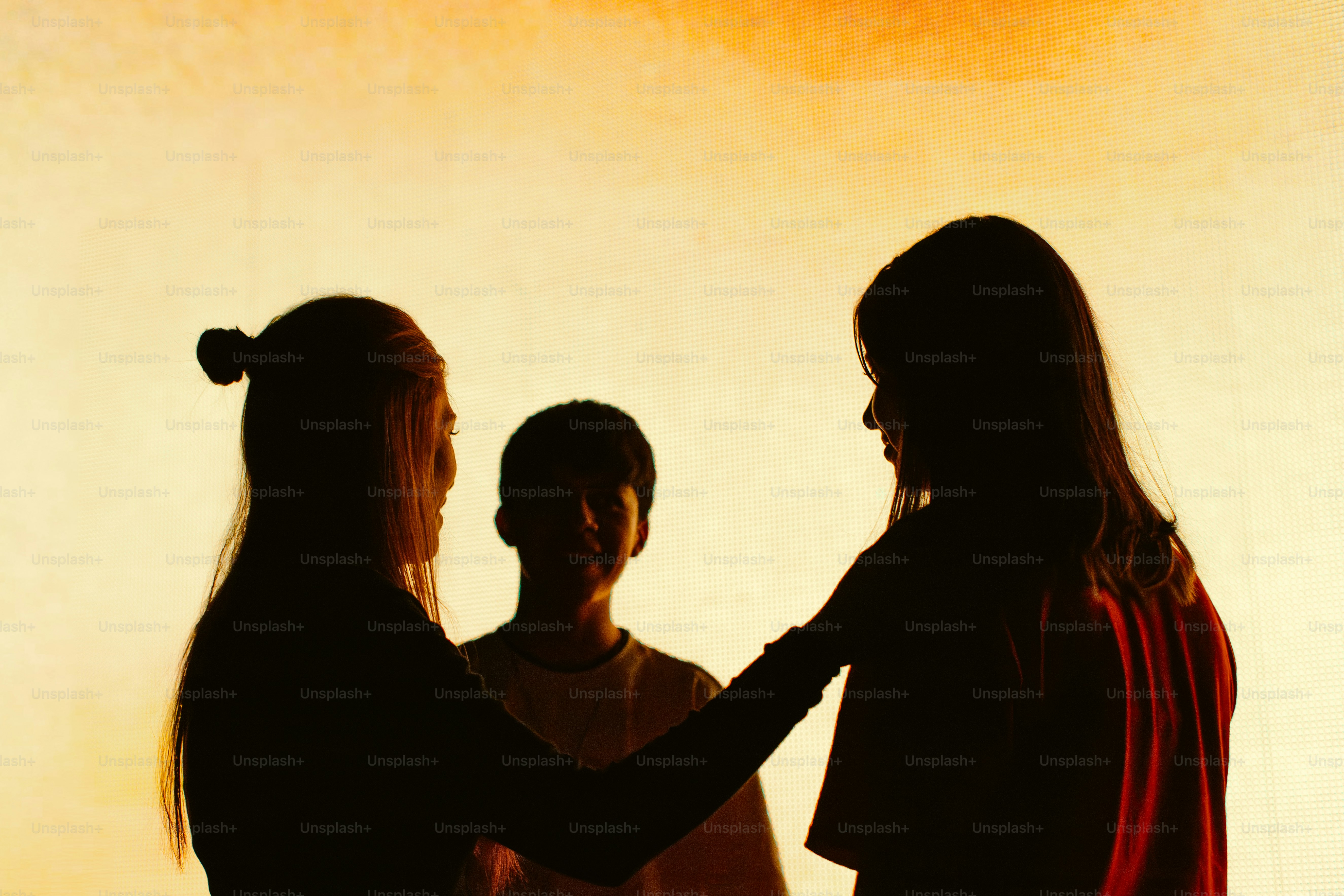 Three people silhouetted against a warm orange sky.