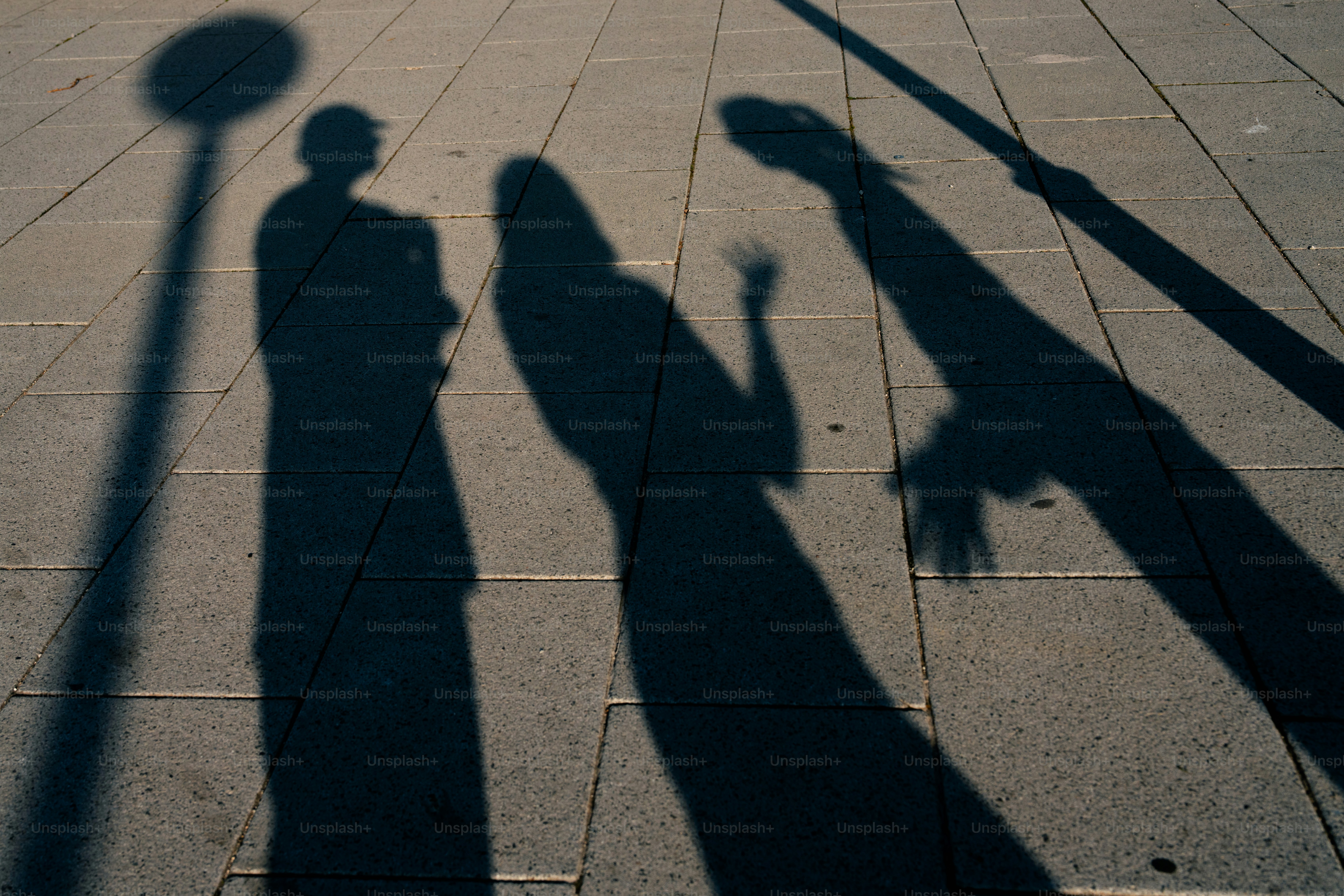 Sombras de tres personas sobre una superficie pavimentada.