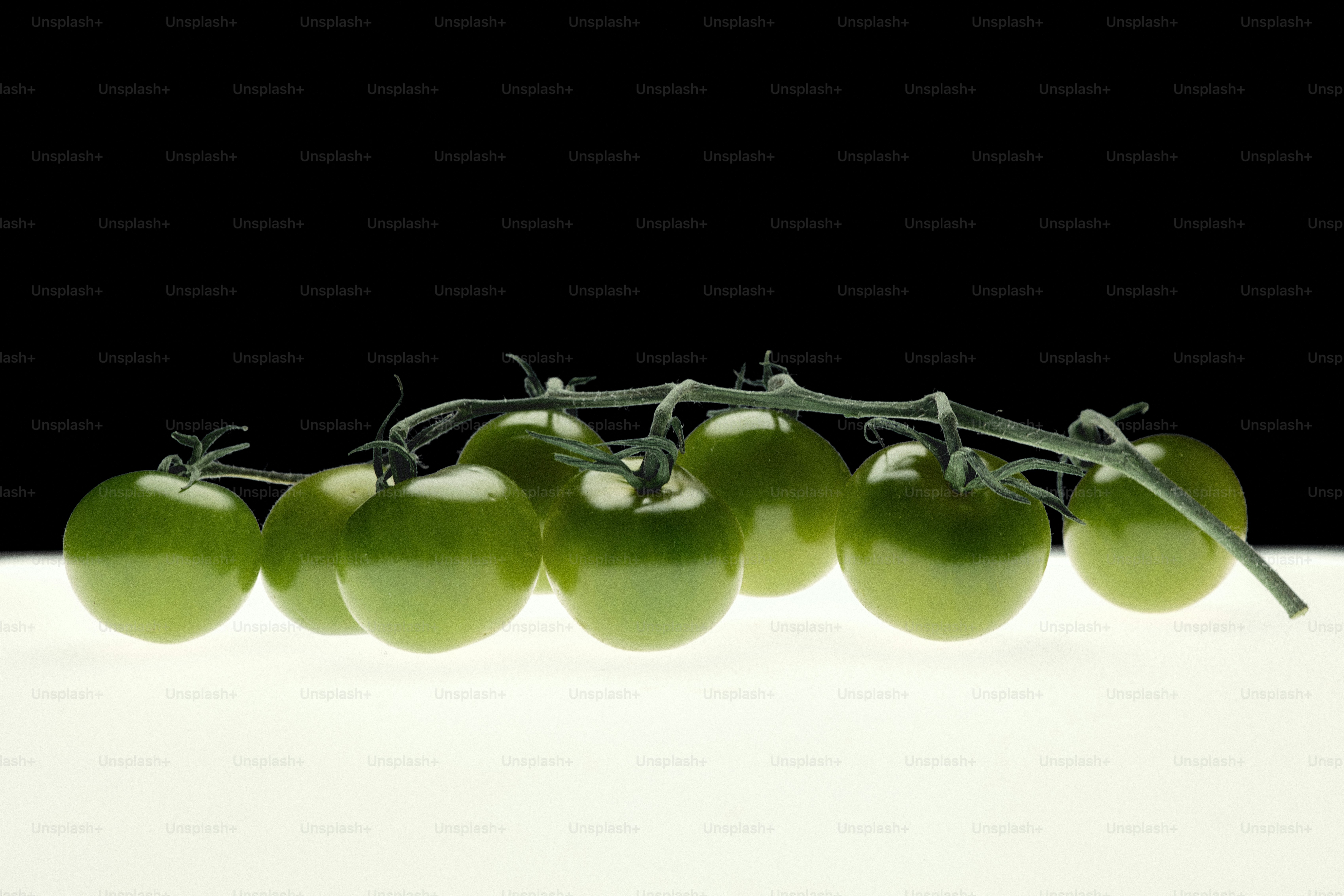 Una enredadera de tomates verdes inmaduros sobre una superficie blanca.