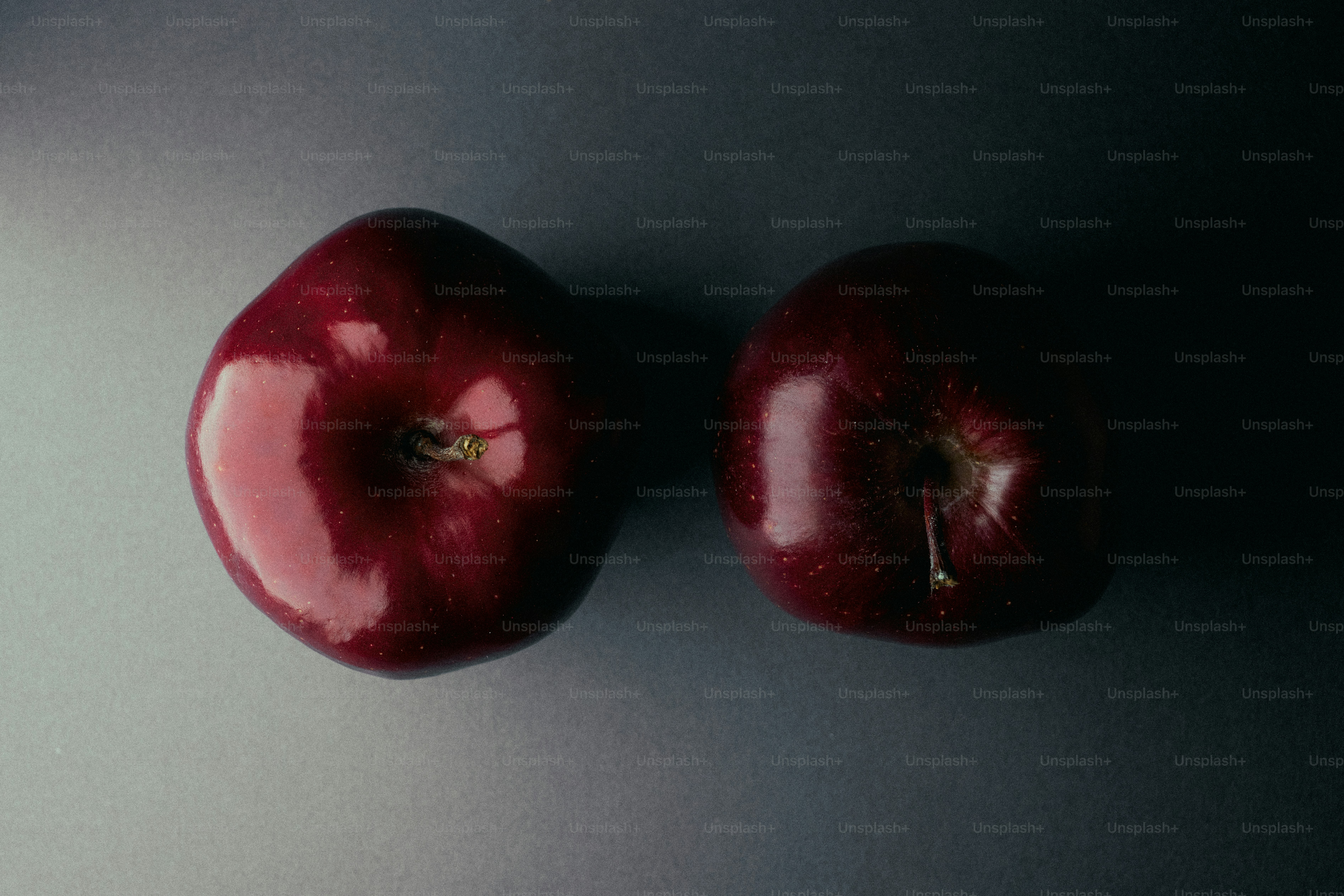 Two shiny red apples on a gray surface