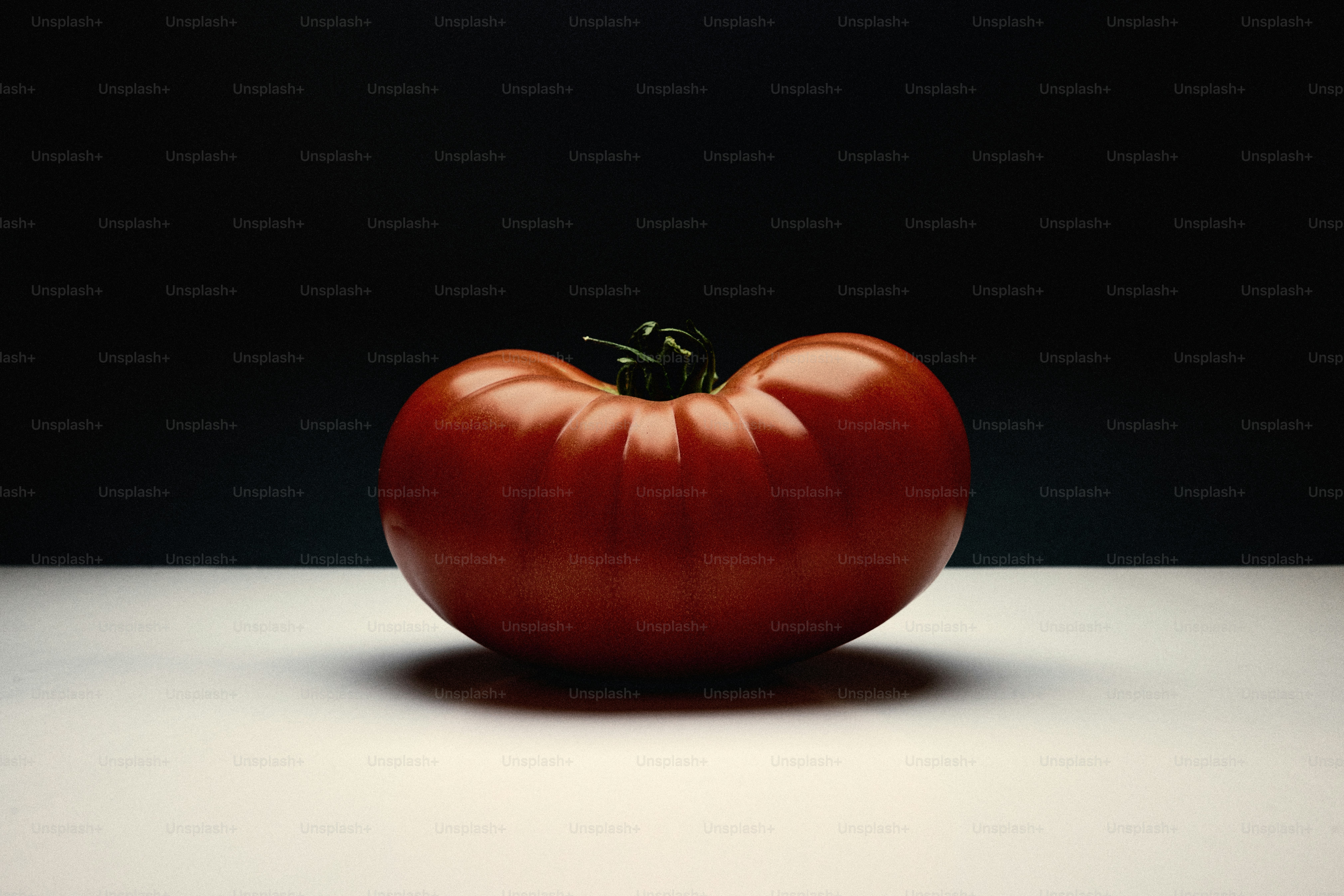 Un solo tomate maduro sobre una superficie blanca.