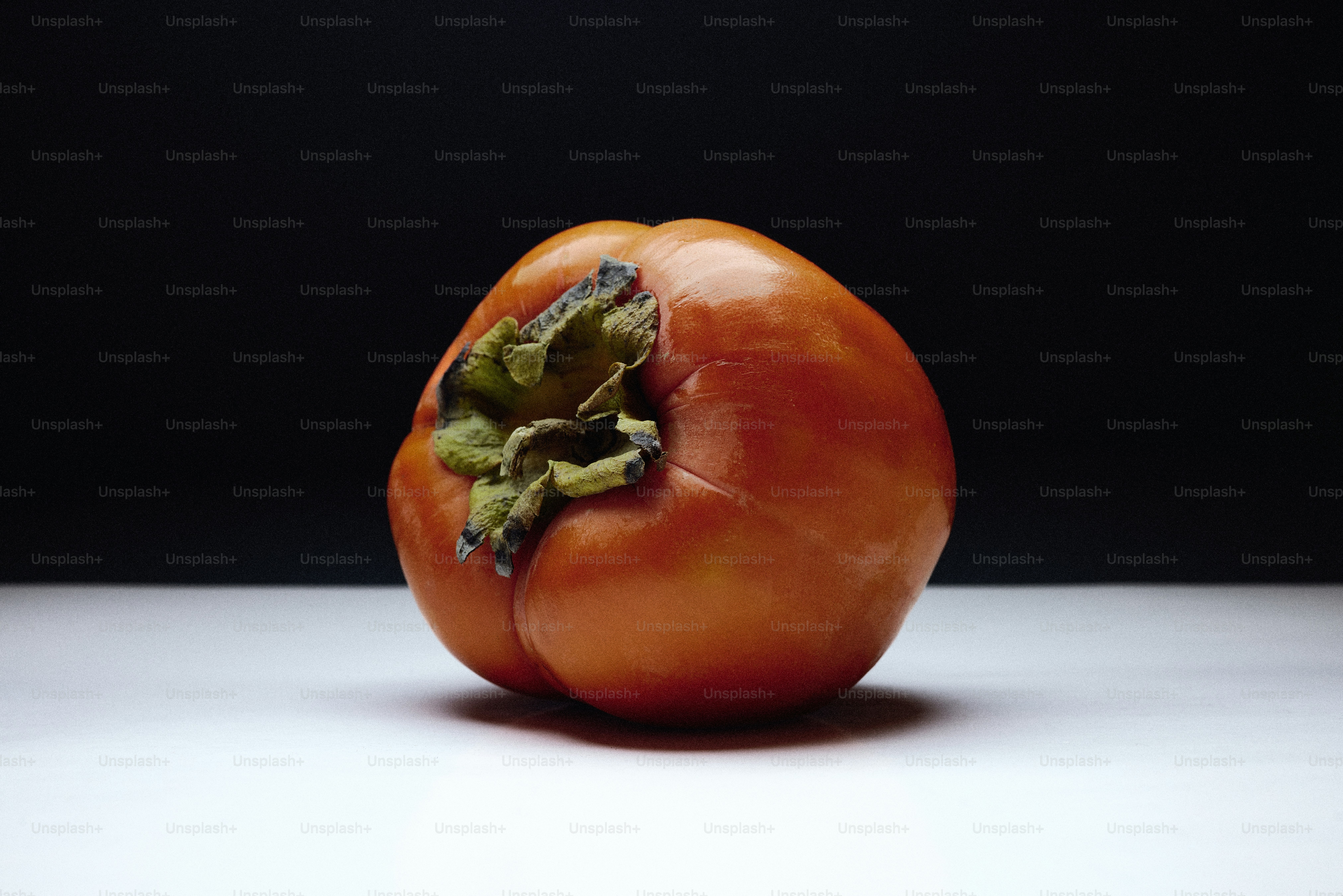 A single ripe persimmon rests on a white surface. photo – Food Image on ...