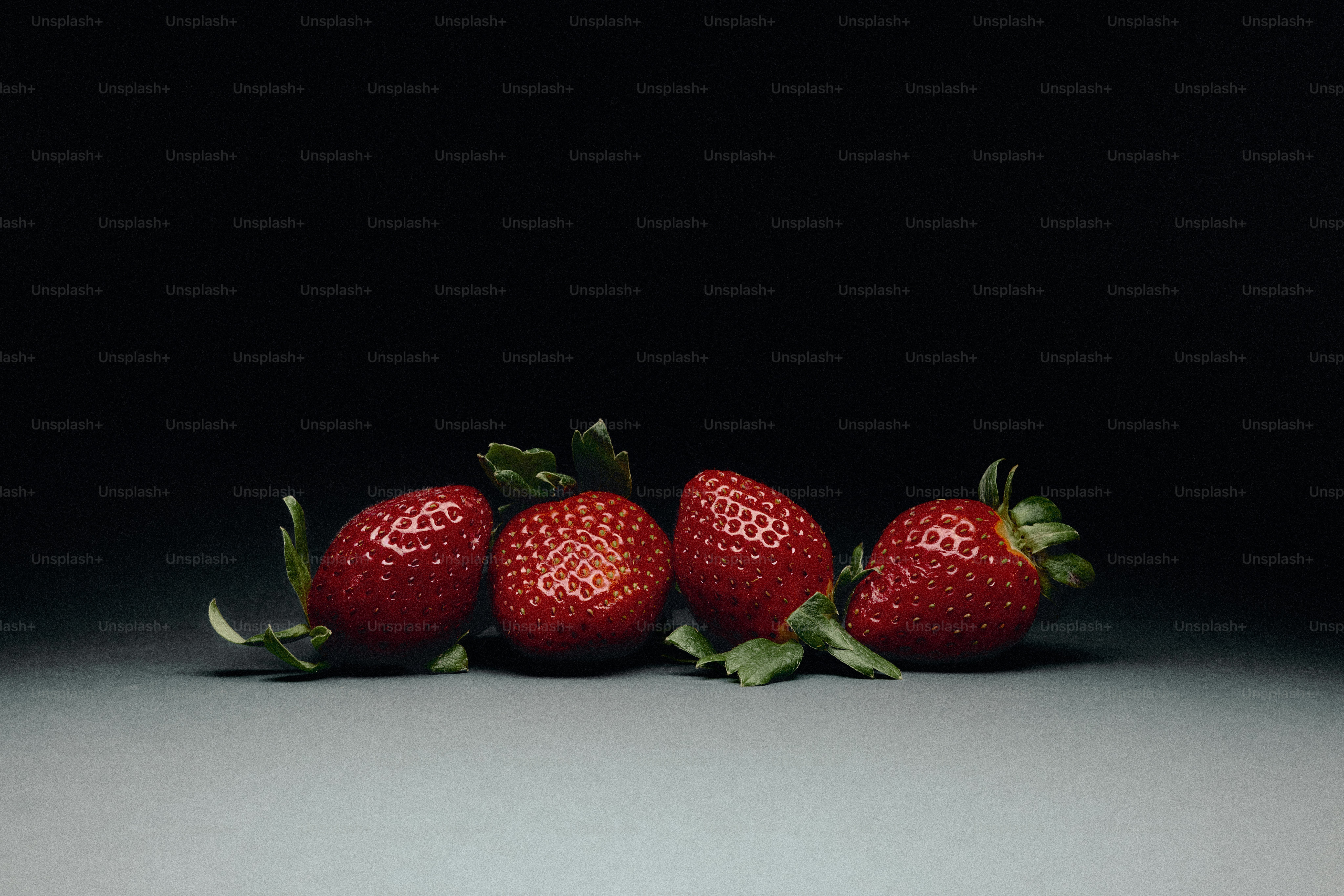 Cuatro fresas maduras con hojas verdes sobre fondo oscuro.