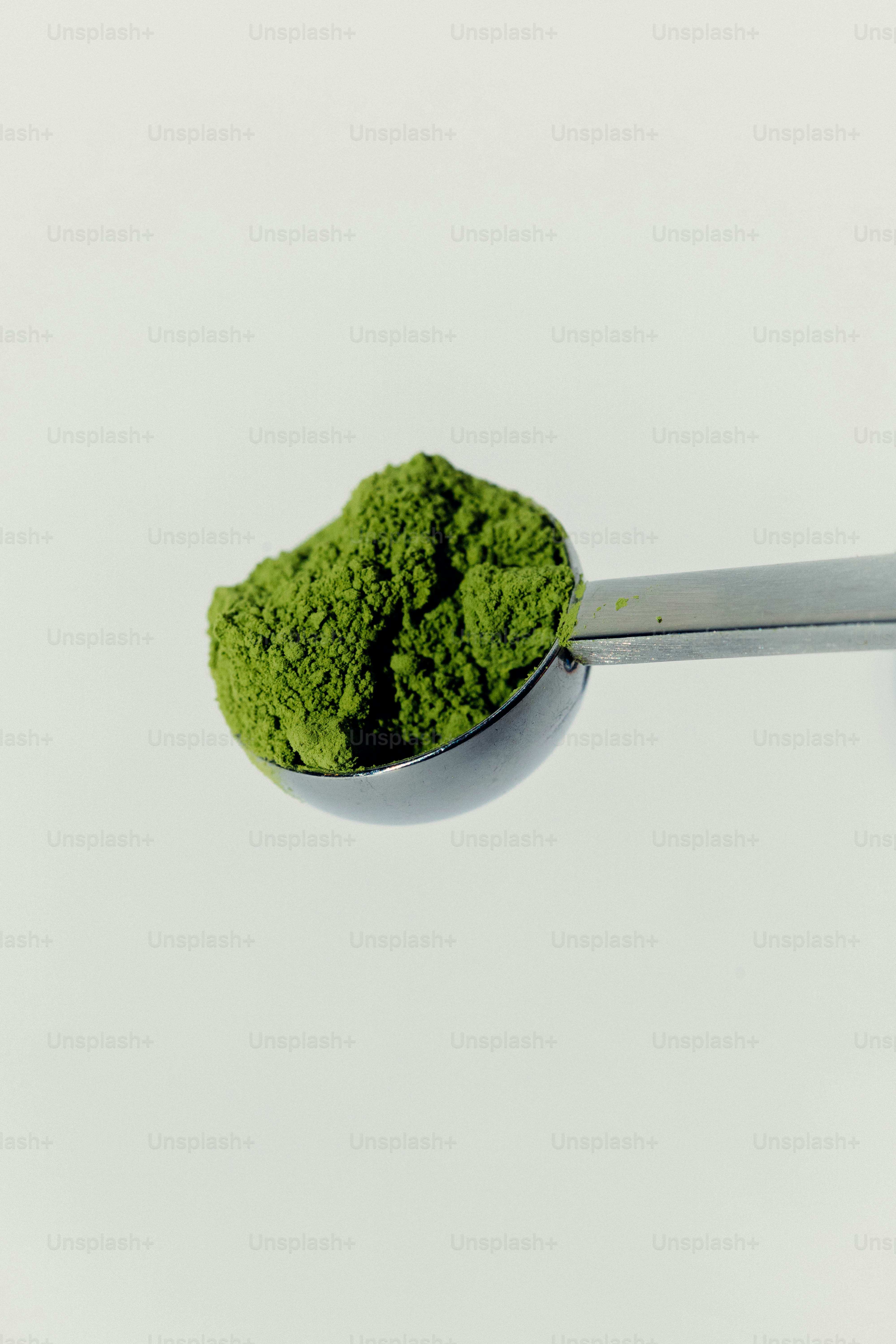 금속 숟가락에는 초록색 말차 가루 더미가 담겨 있습니다.