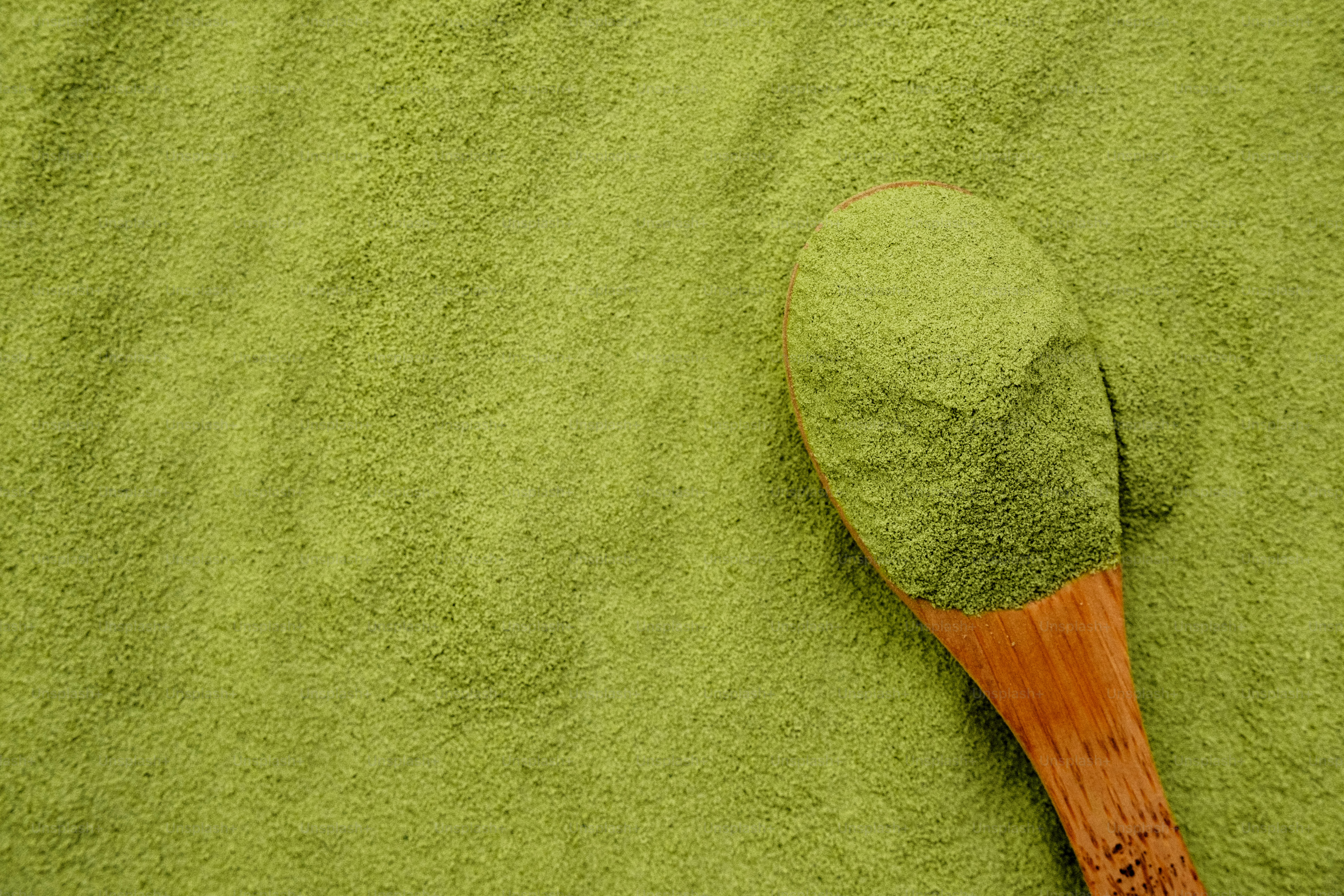 Wooden spoon with green powder on a green background
