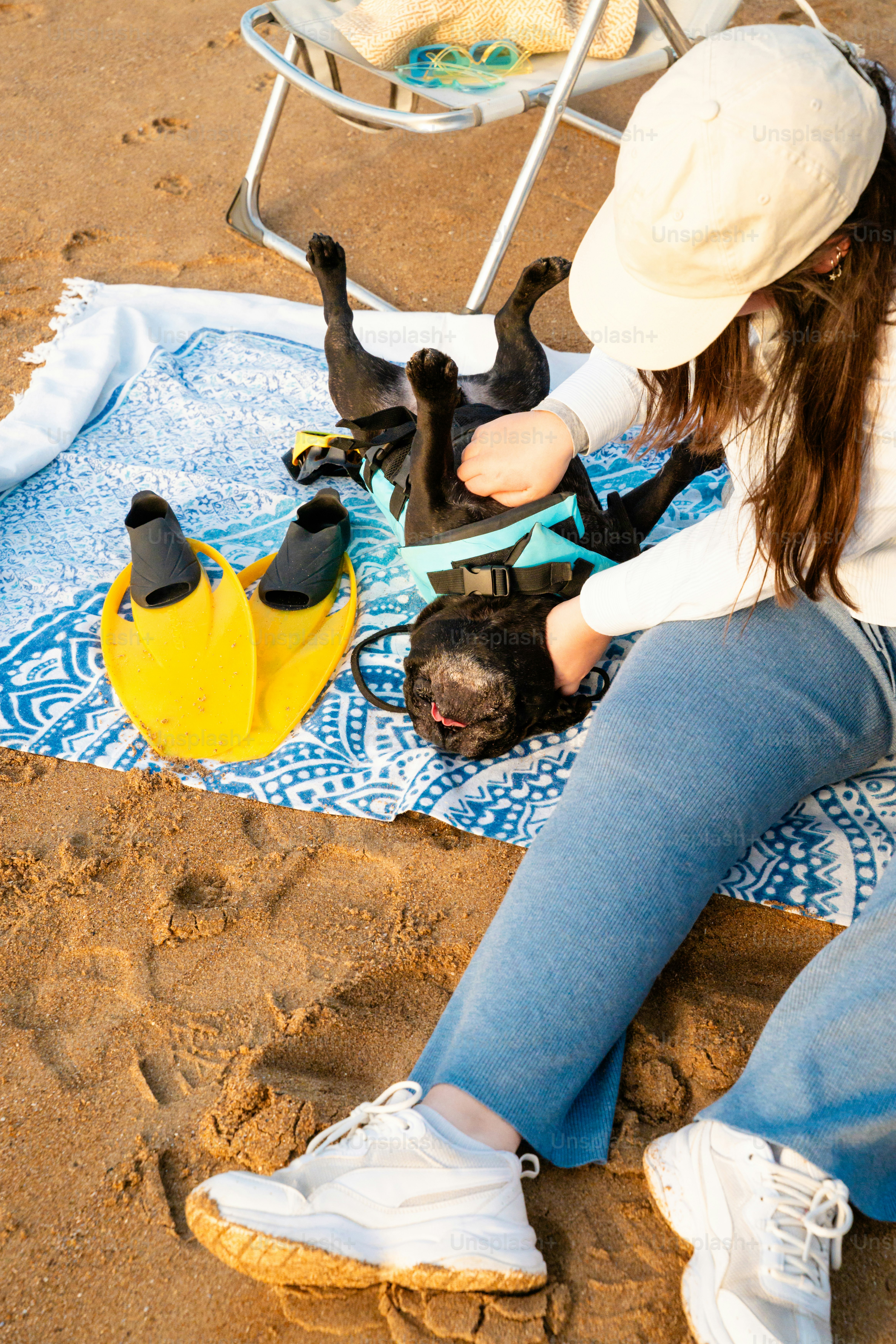 Woman petting a black french bulldog on a beach blanket.