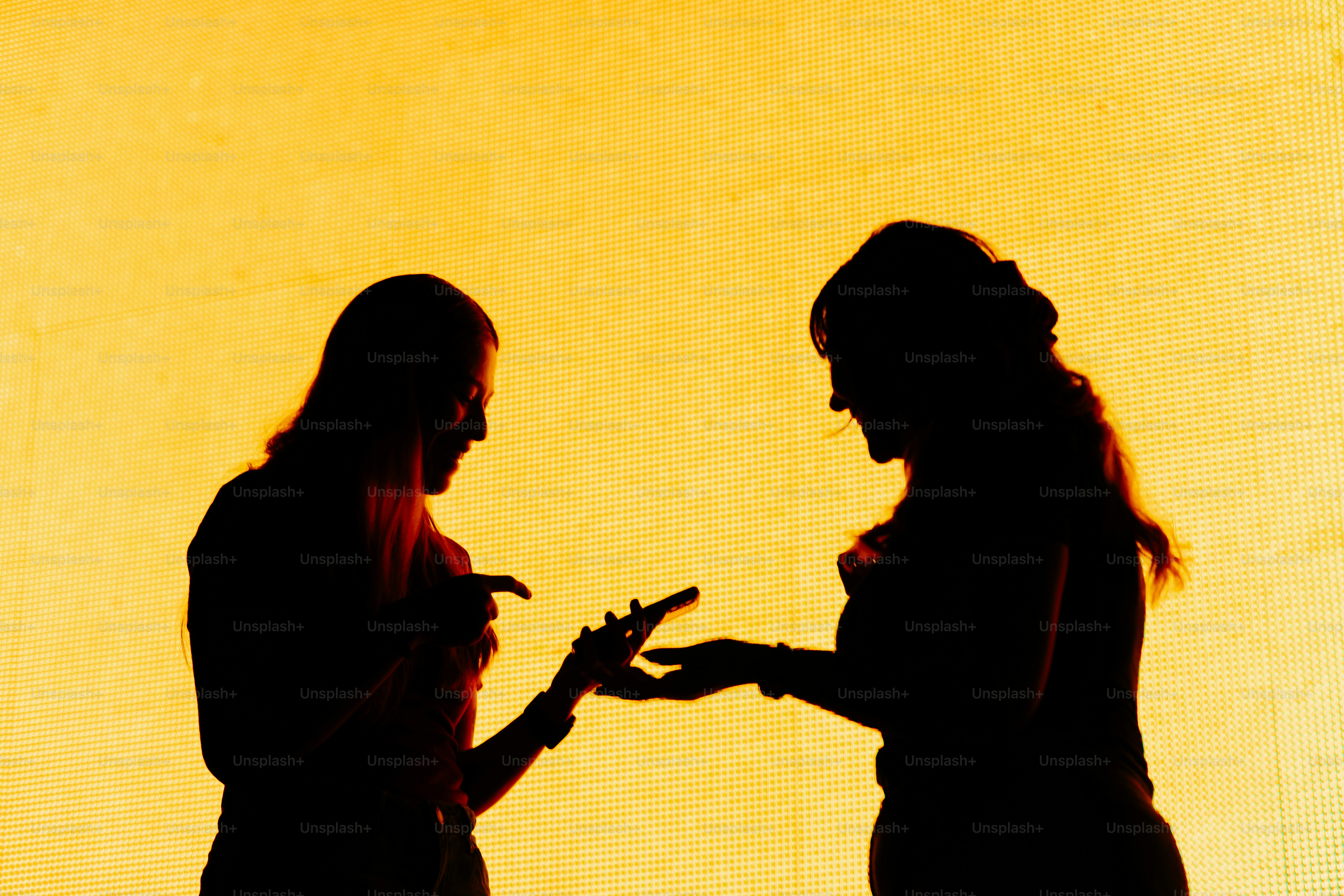 Two women in silhouette talking against yellow background.