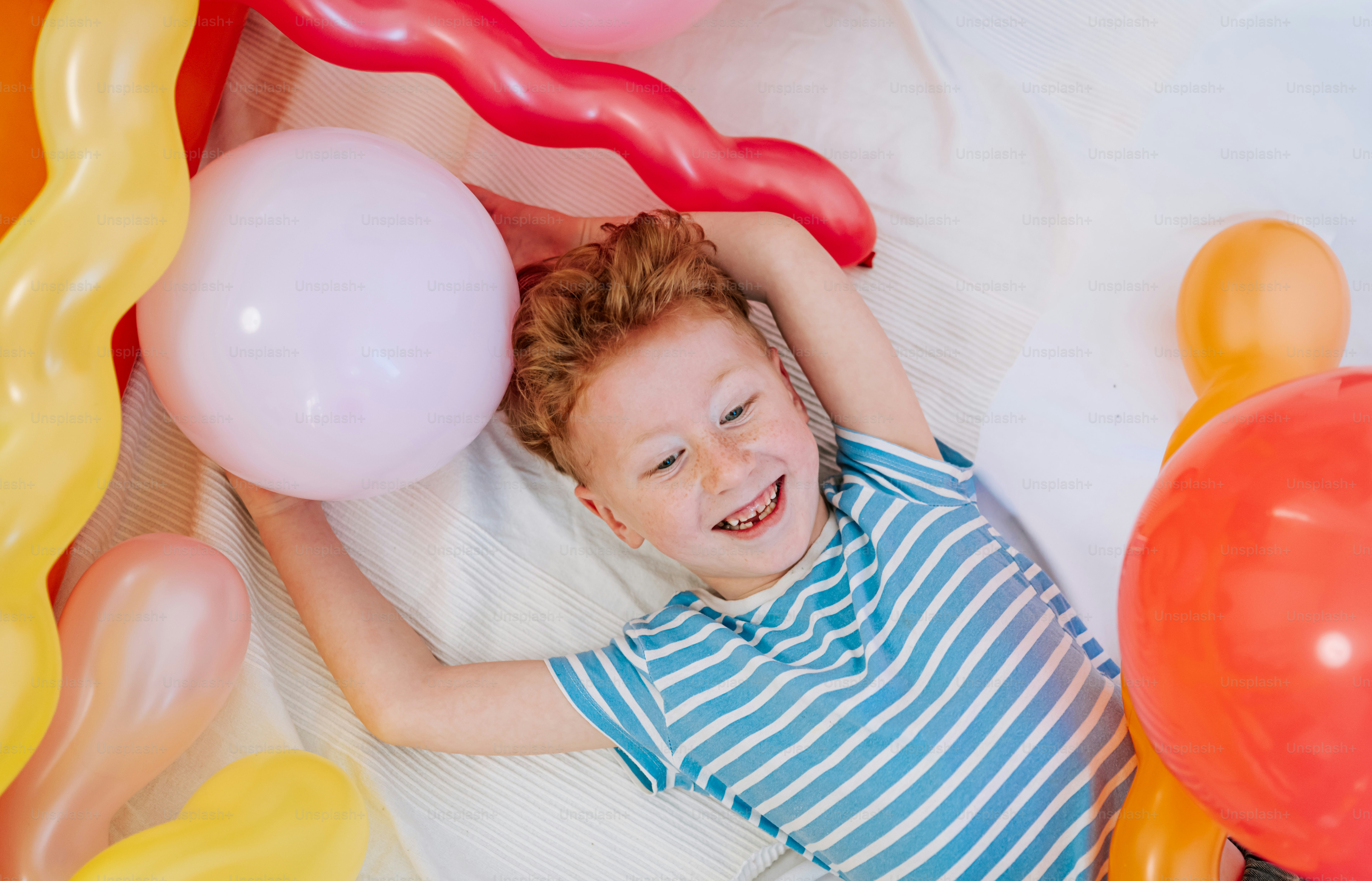 A happy boy lying among colorful balloons