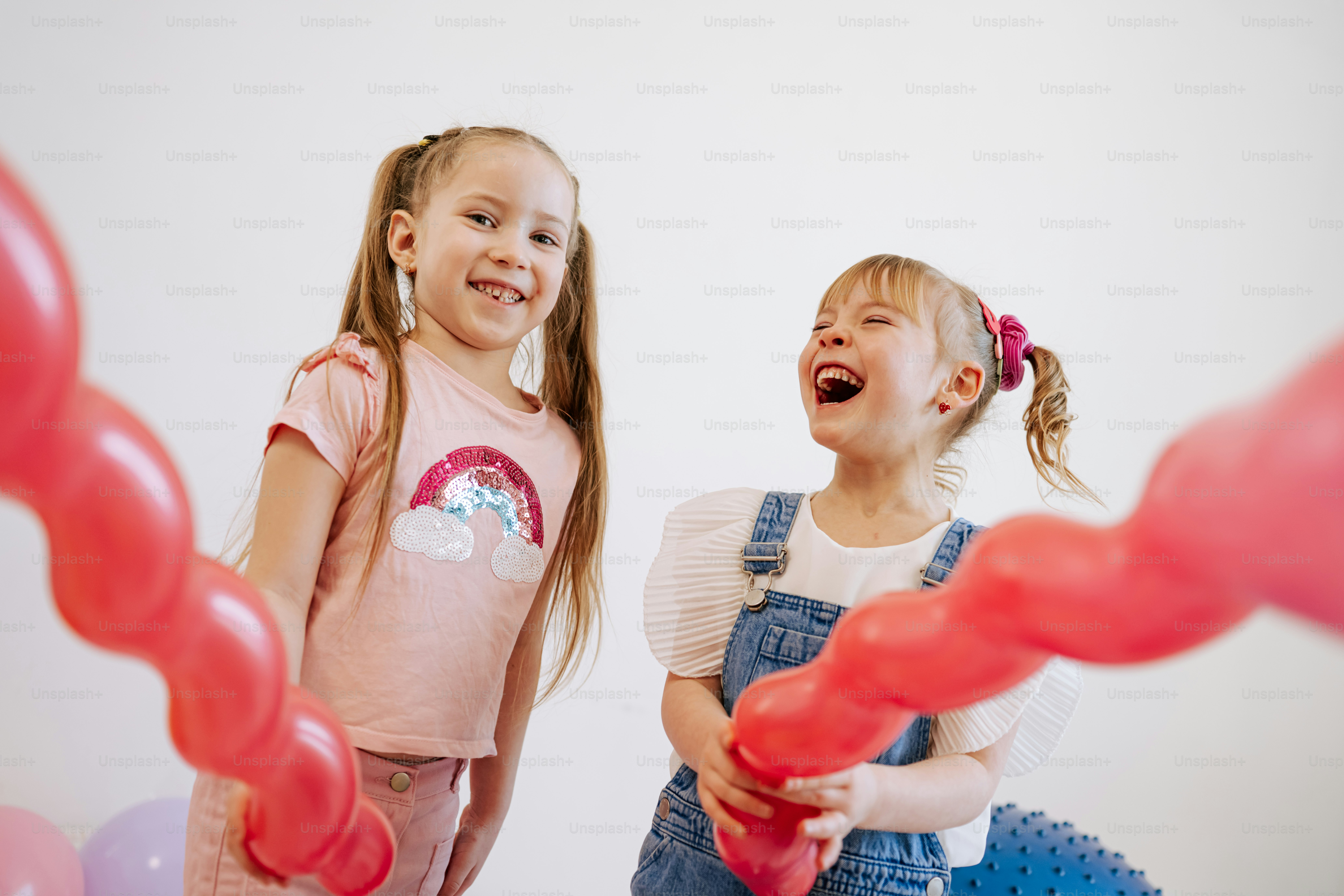 Two happy girls playing with red balloons.
