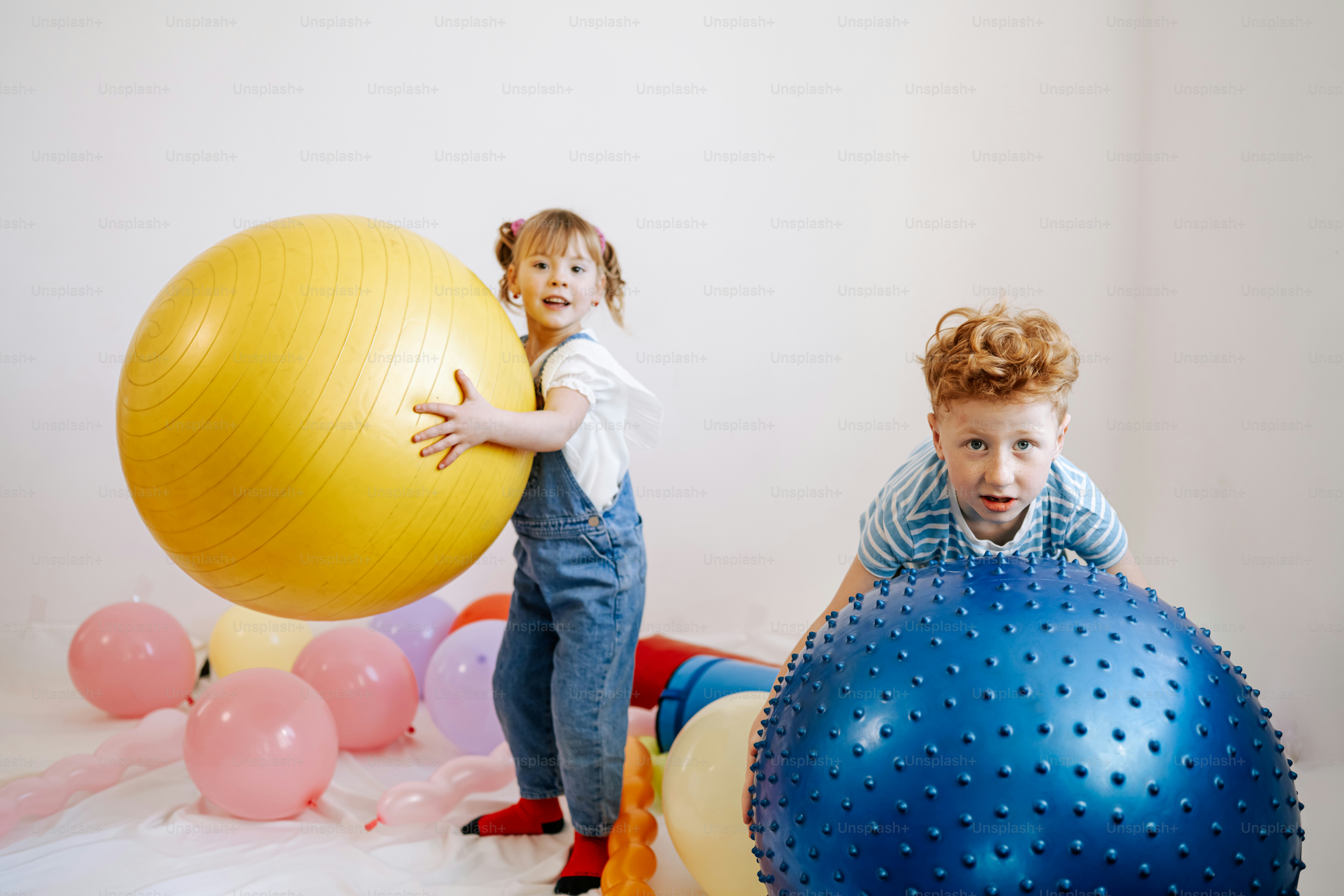 Two children with large exercise balls and balloons