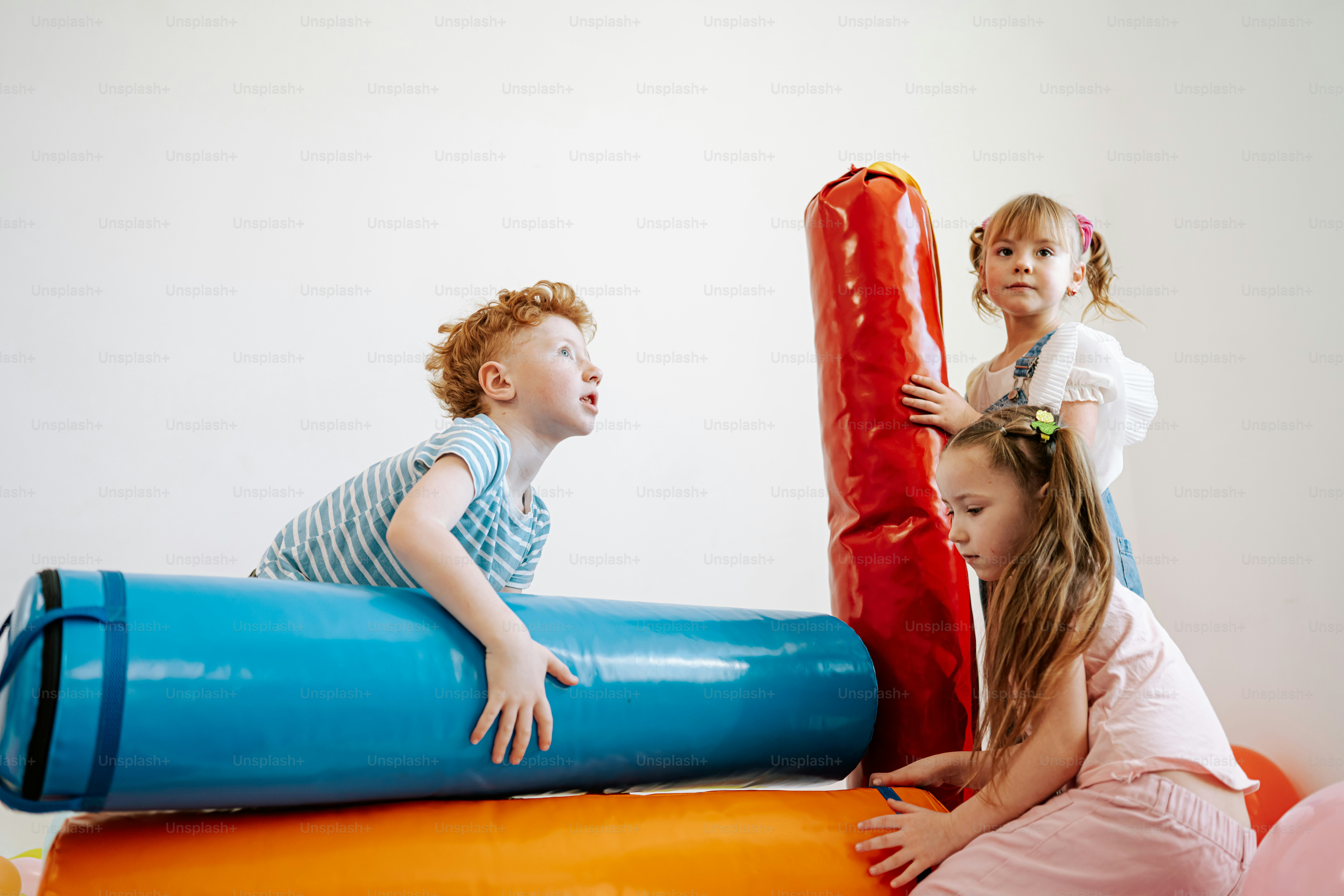 Three children playing with colorful foam rollers