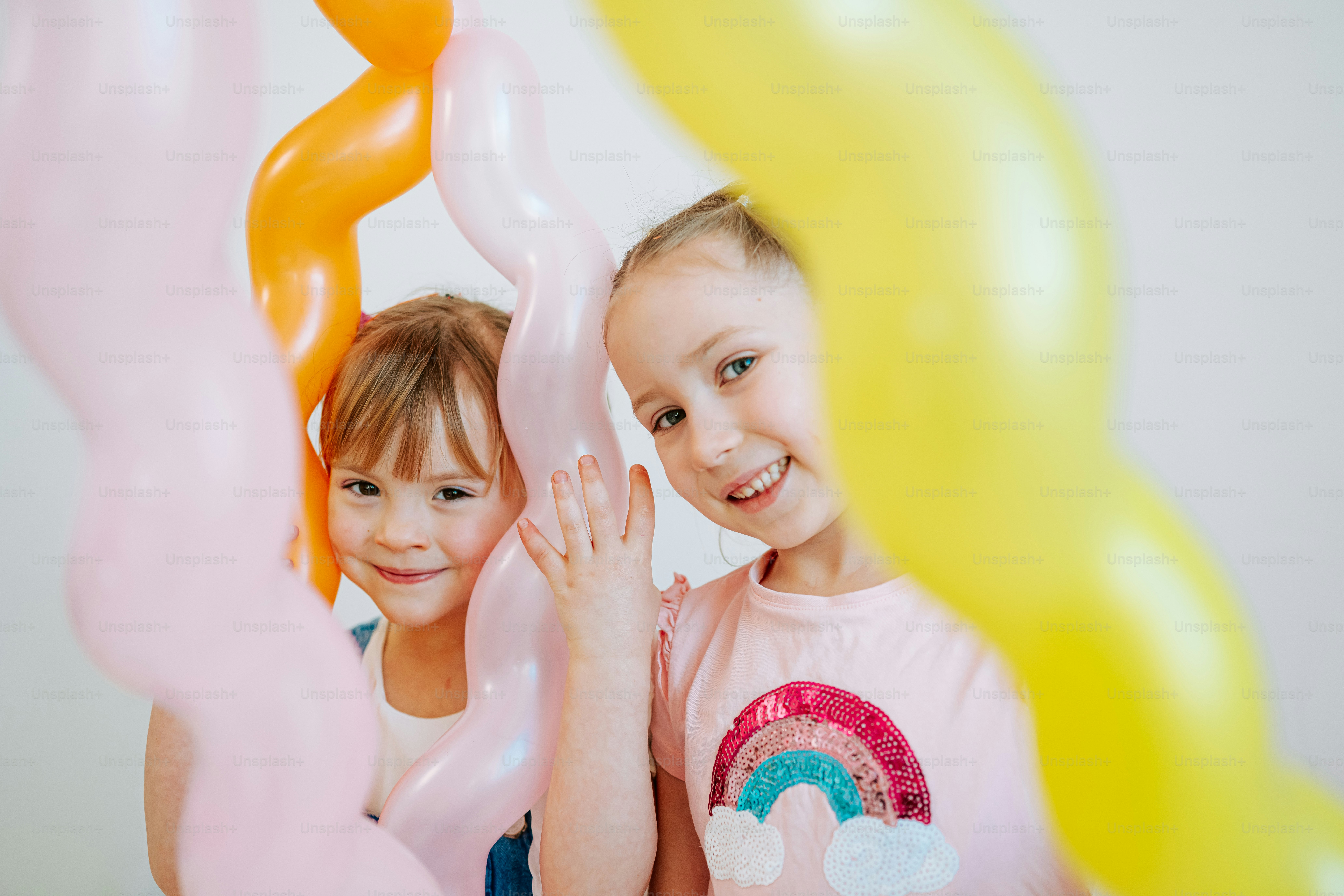 Two smiling girls behind colorful balloons