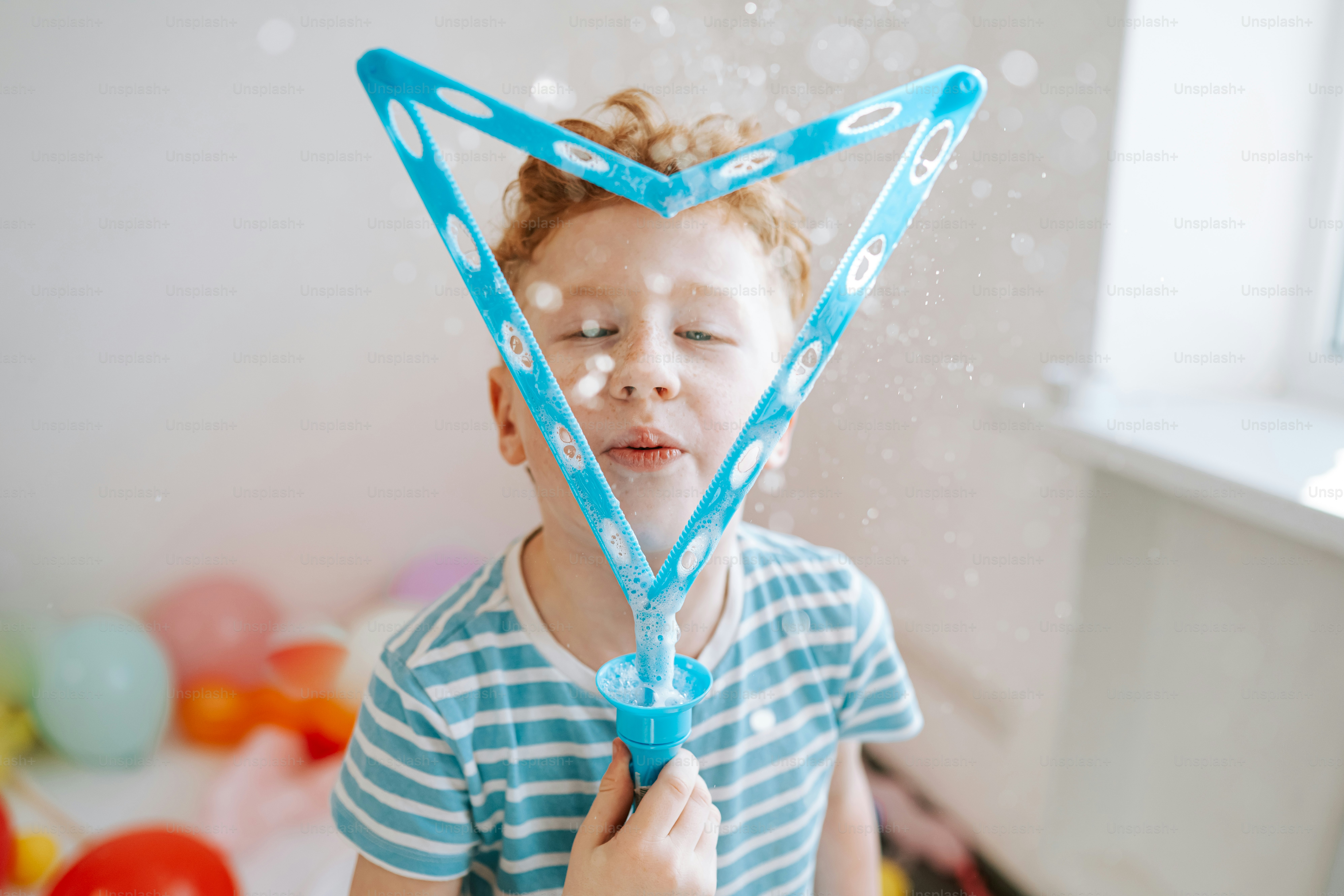 A young boy blowing bubbles with a triangular wand.