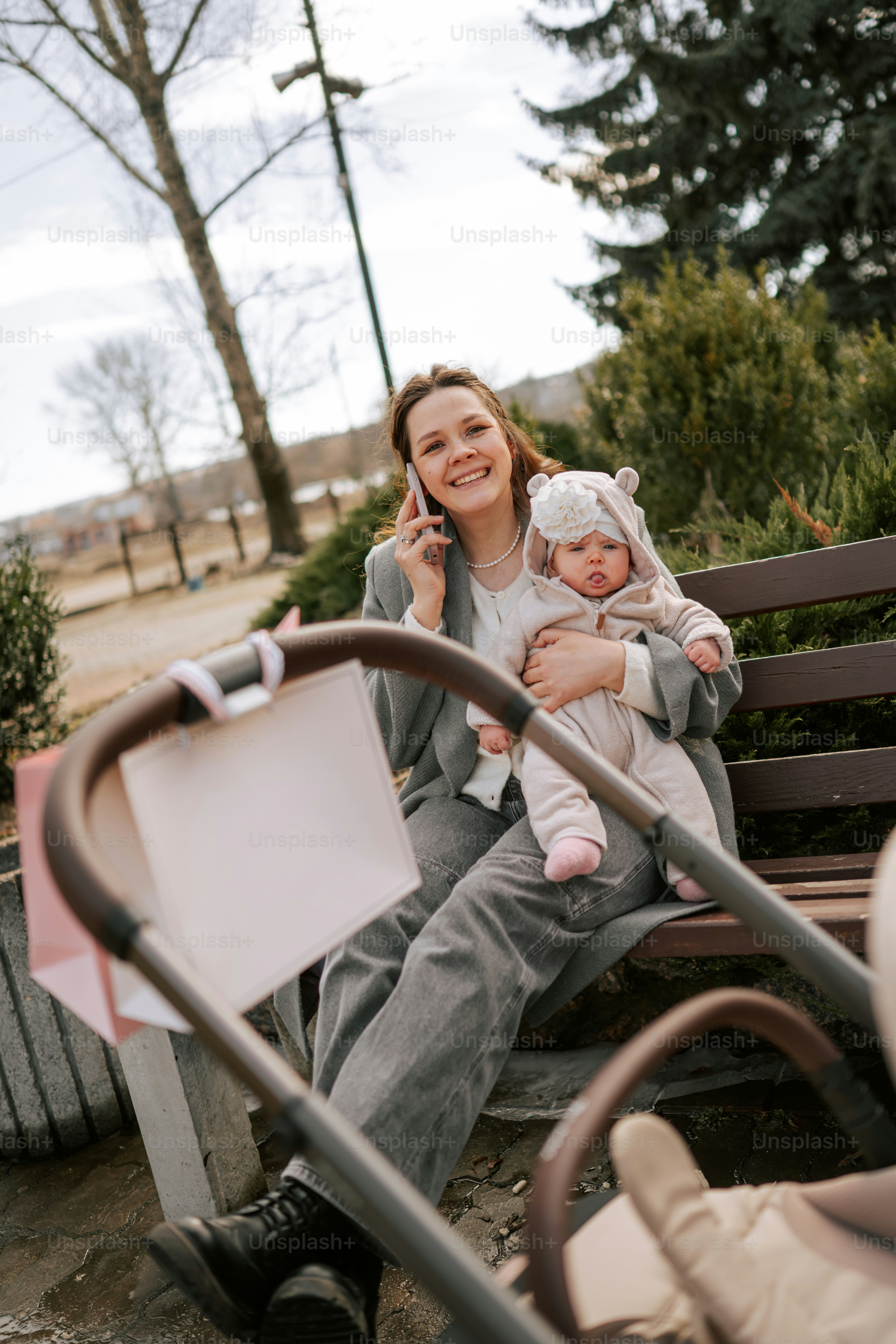 Woman on bench holding baby, talking on phone.