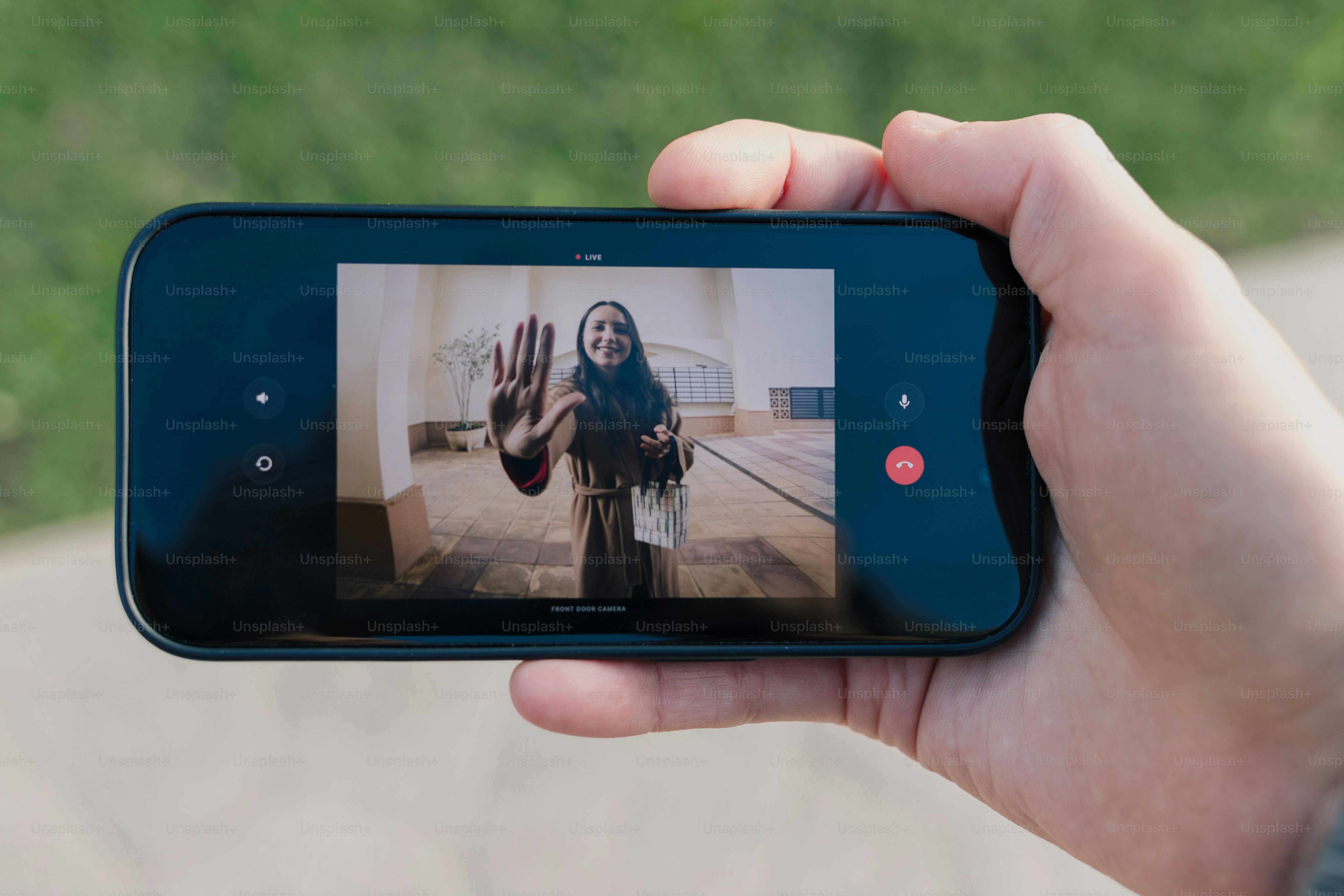 Person holding a smartphone displaying a woman waving hello