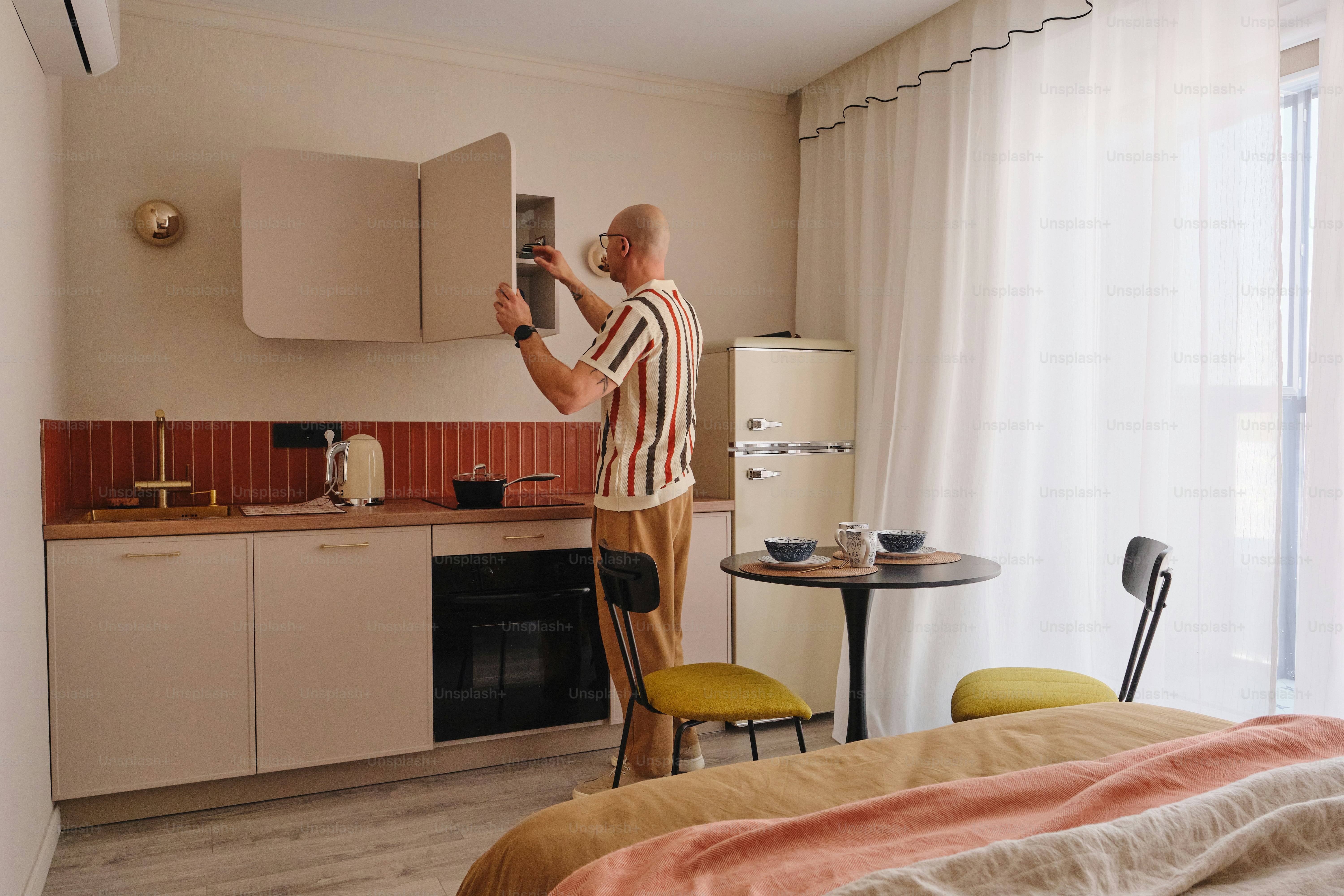 Un homme ouvrant un placard dans une petite cuisine studio.