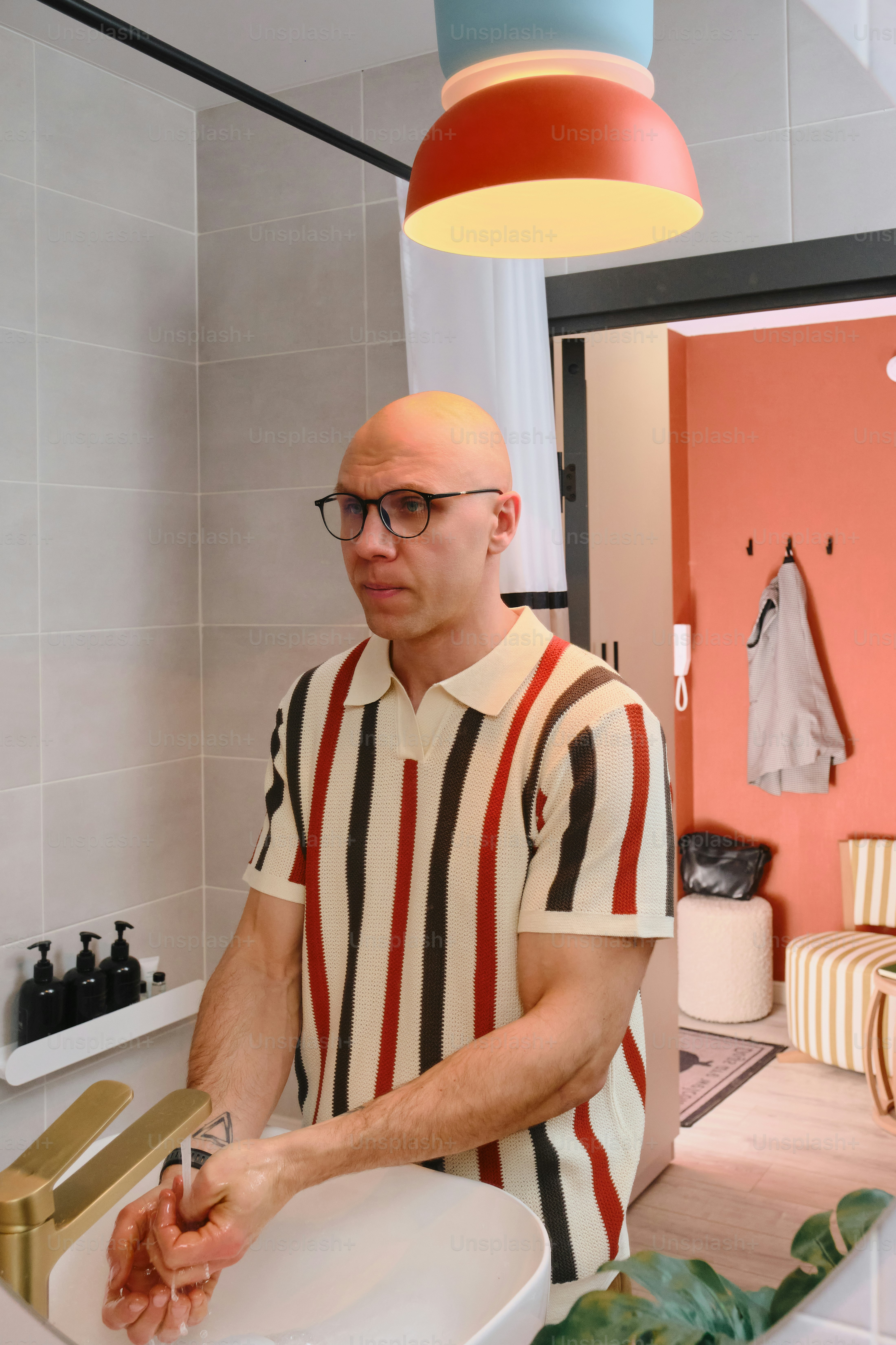 Bald man with glasses washing hands at sink