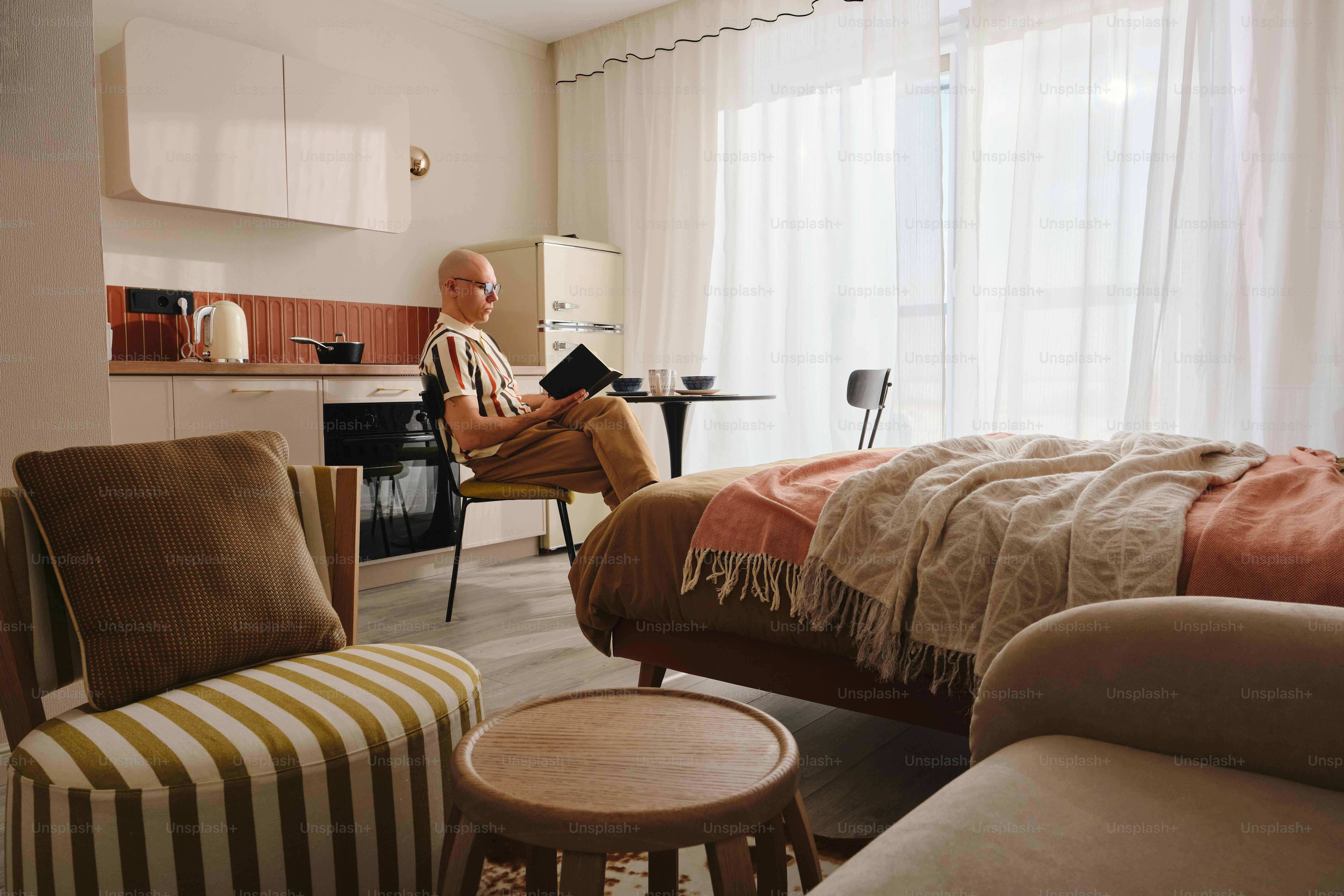 Man sitting in a studio apartment with kitchen and bed.