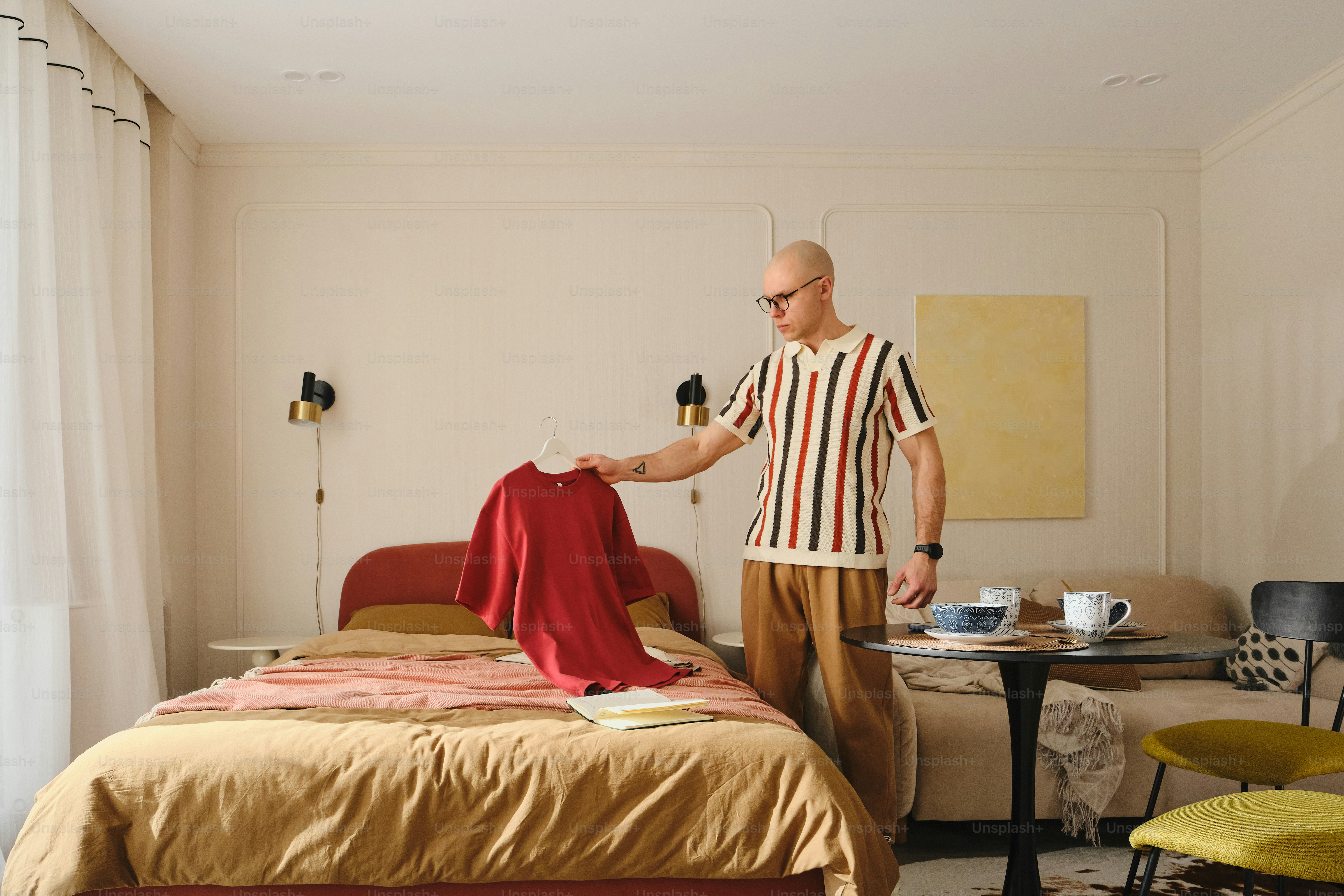 Man holding red shirt over a bed