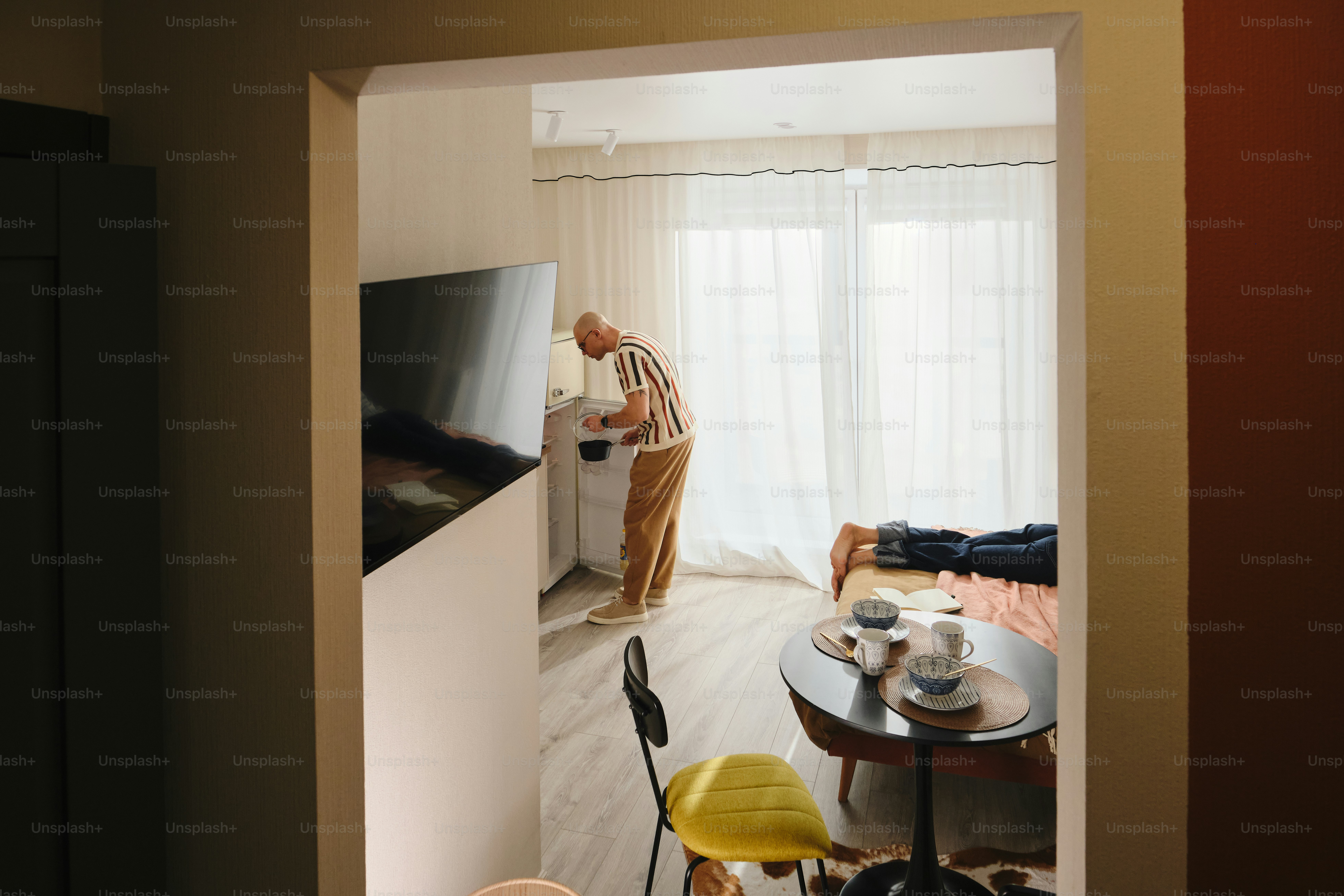 Man plugging in a white appliance near a television.