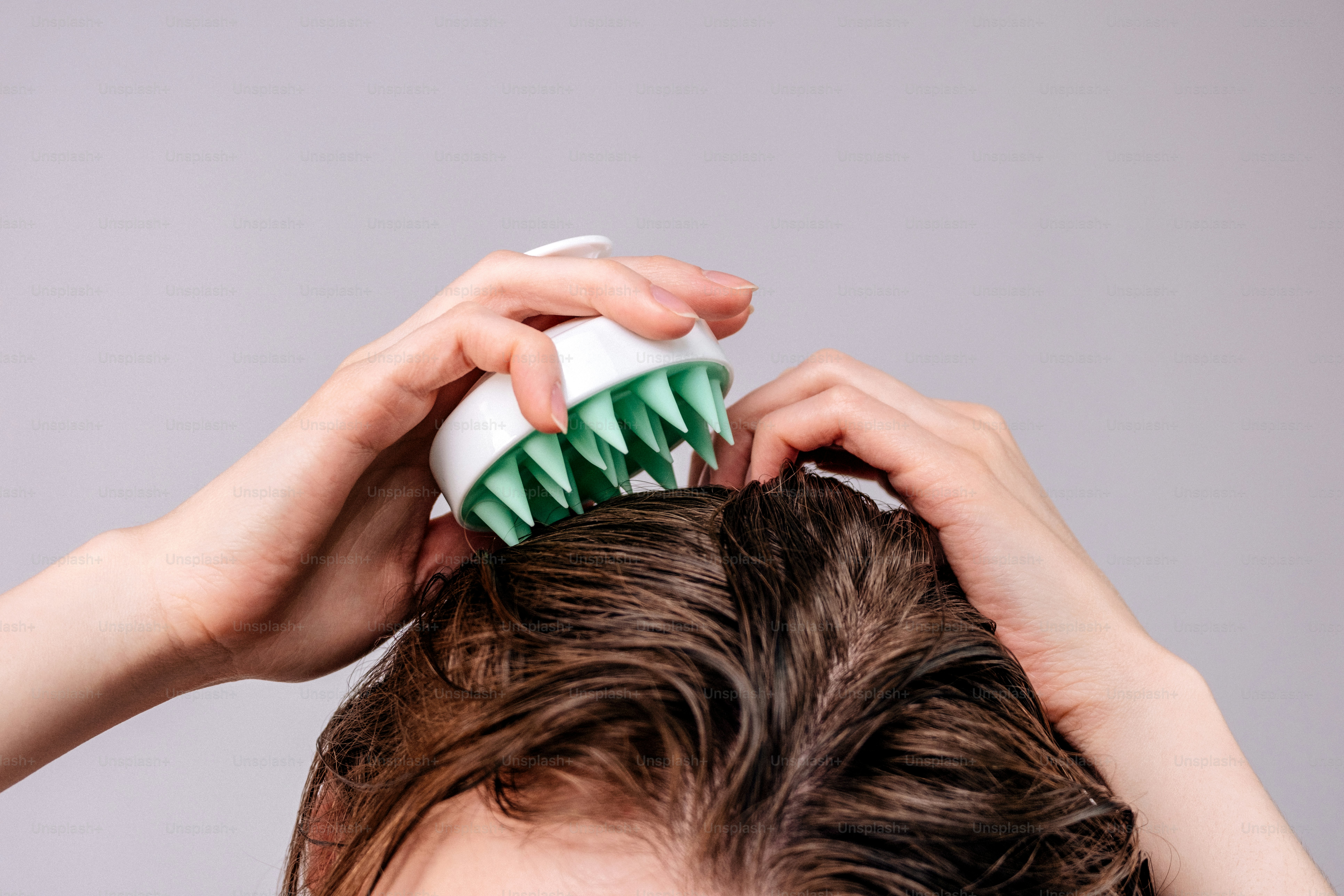 Hands massaging scalp with a green and white brush
