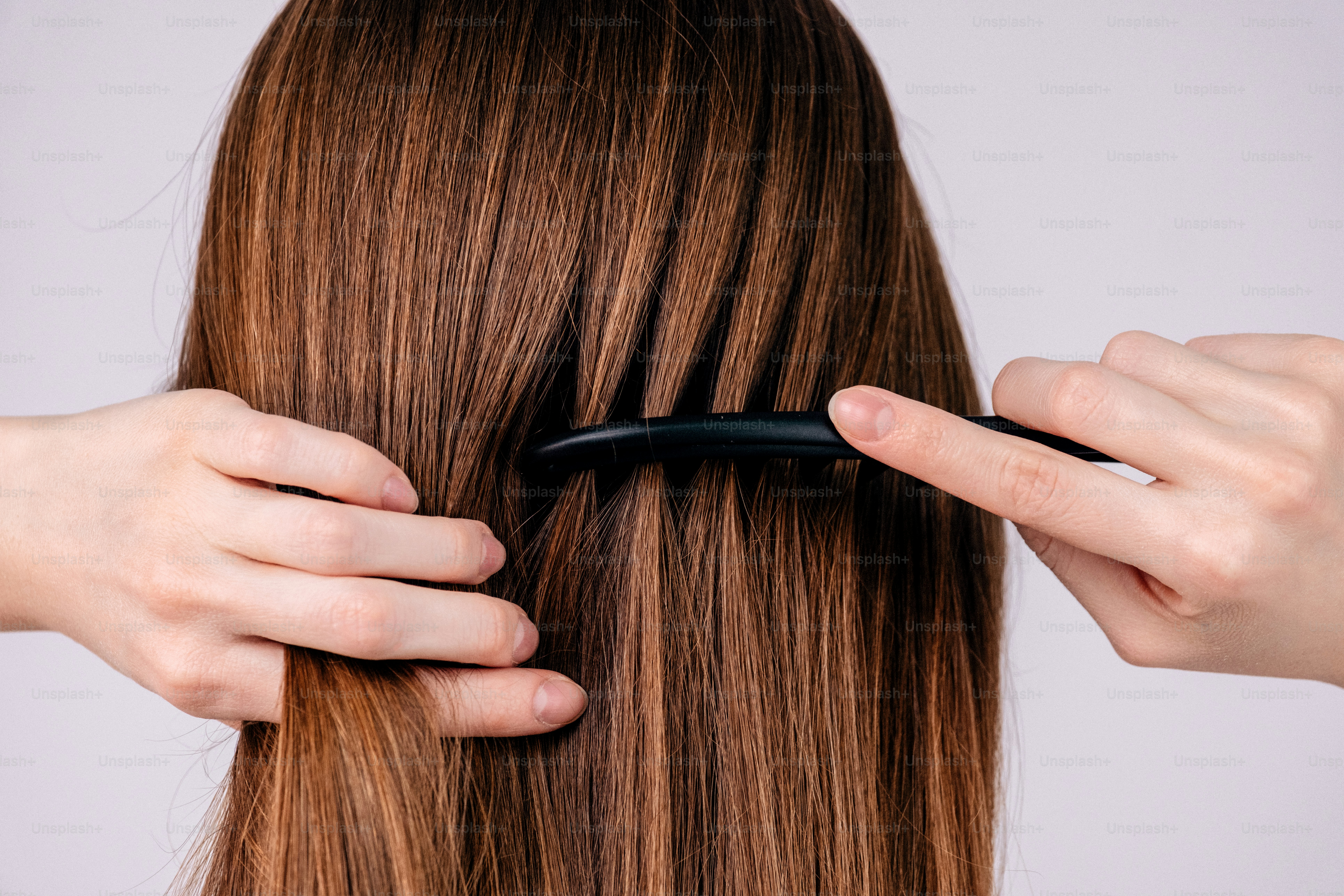 Hands combing long brown hair against a light background