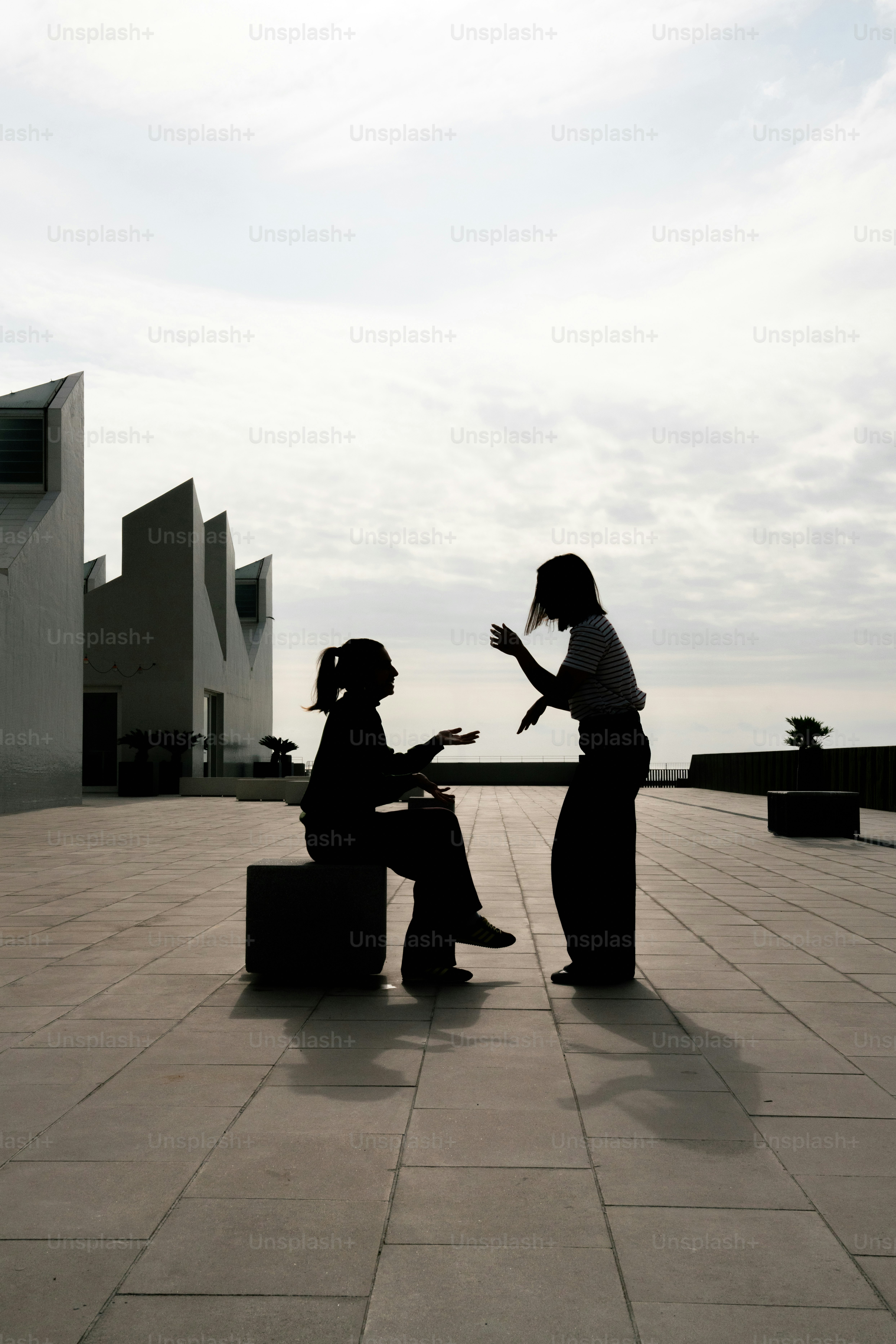 현대 건축물이 있는 옥상 위에 실루엣으로 선 두 사람.