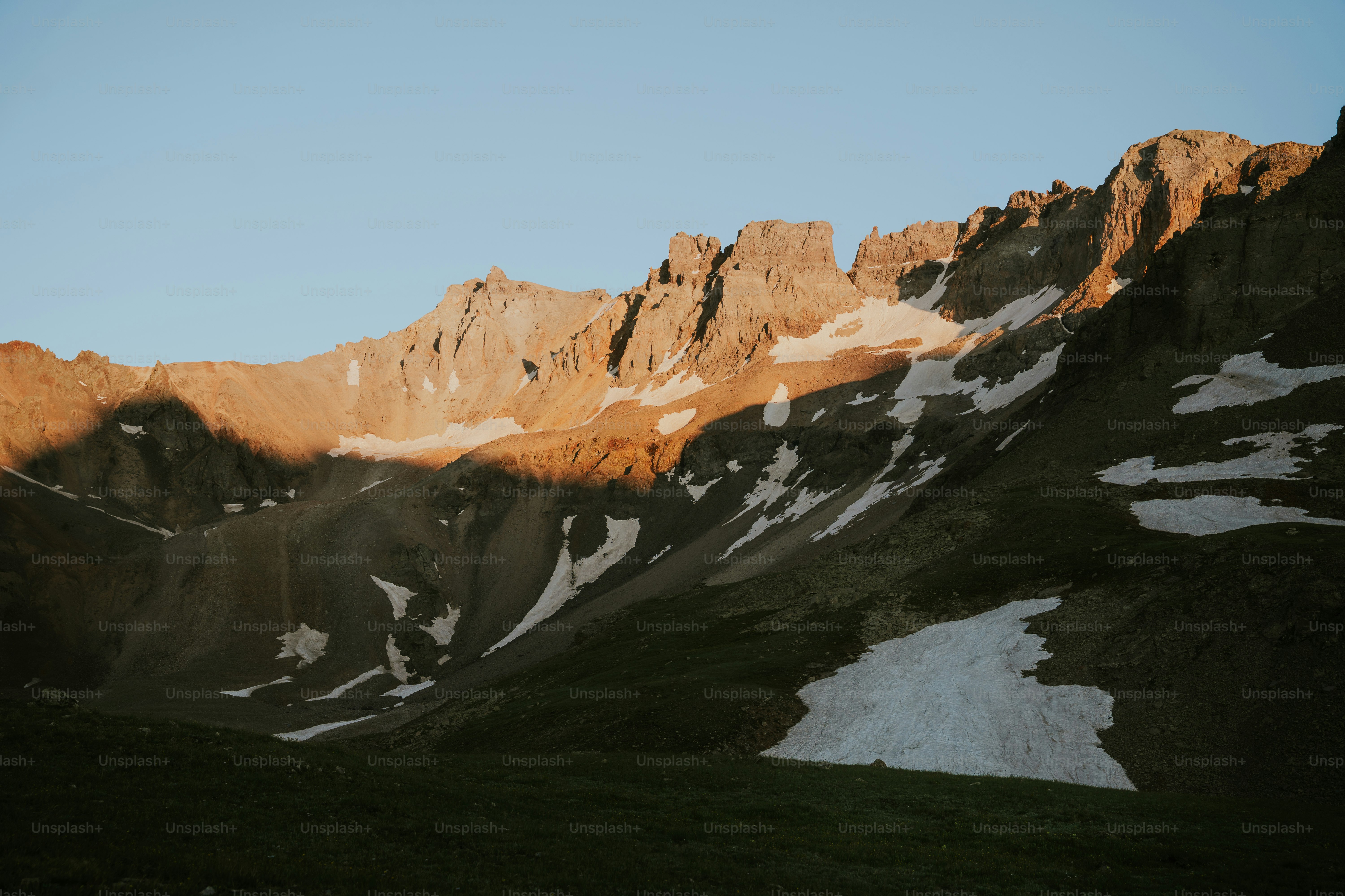 Sunlight illuminates rugged mountain peaks with patches of snow.