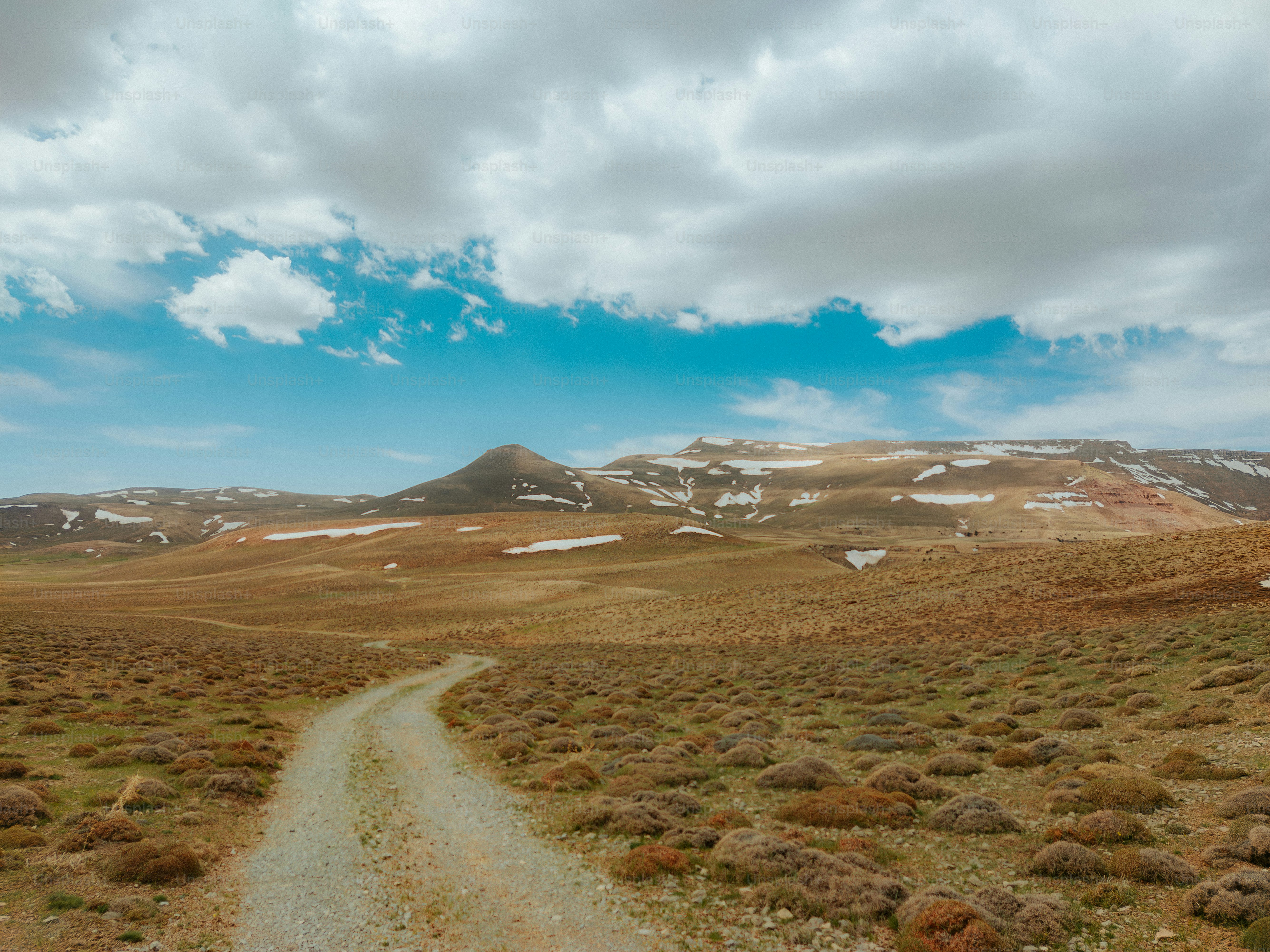 Uma estrada de terra atravessa uma paisagem seca e acidentada.