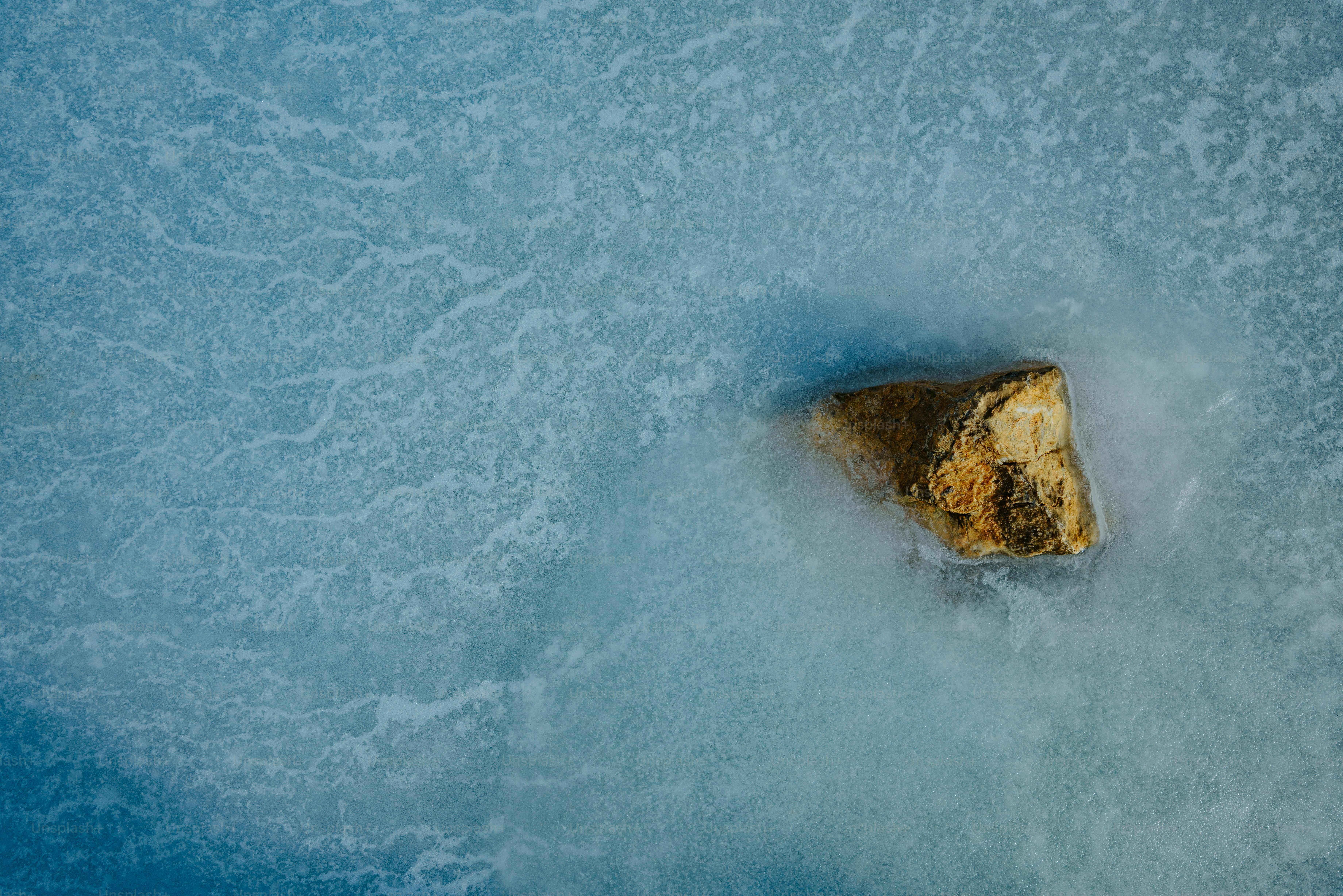 A single rock resting on a frozen blue surface.