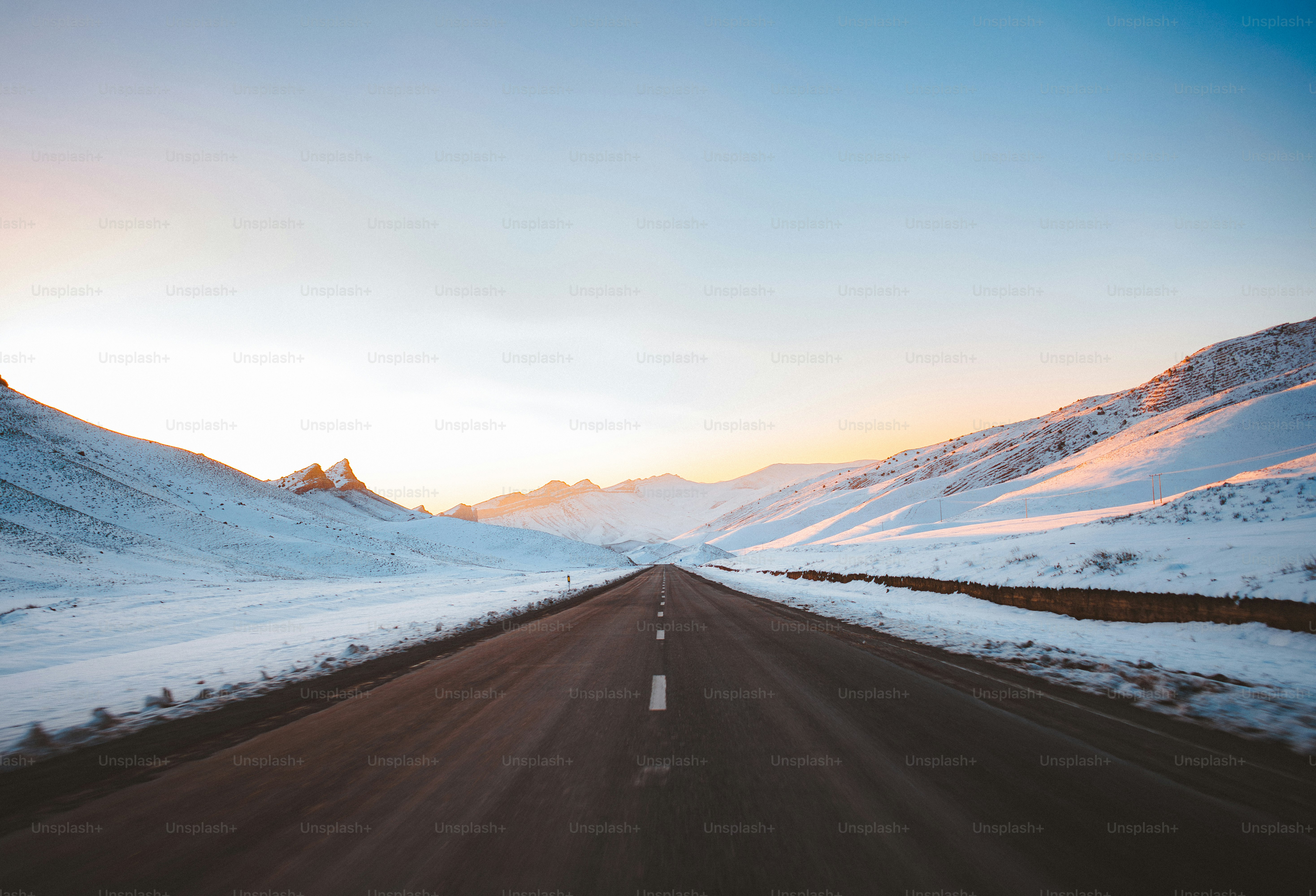Empty road through snow-covered mountains at sunrise