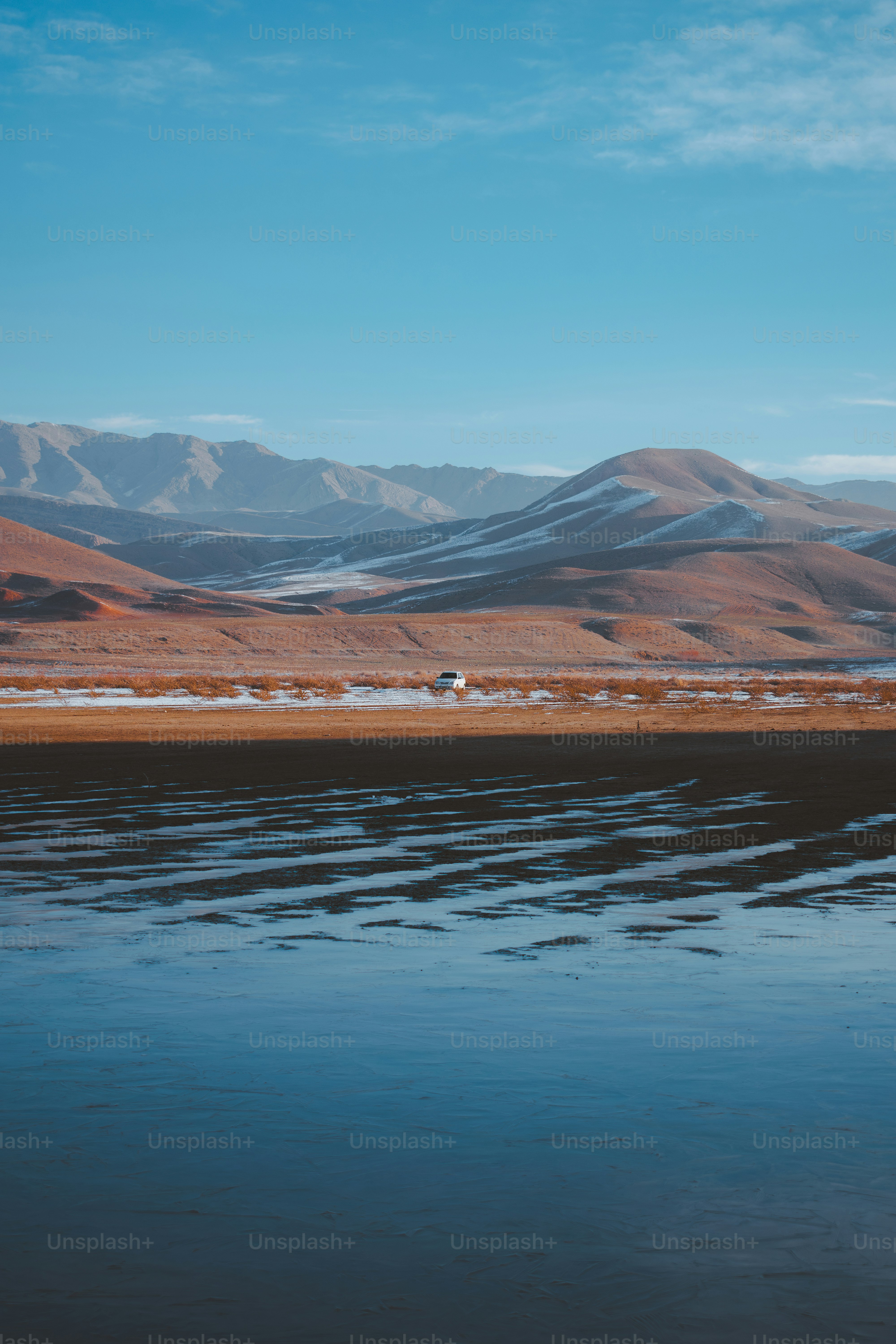 A white vehicle drives along a barren, snow-dusted landscape.