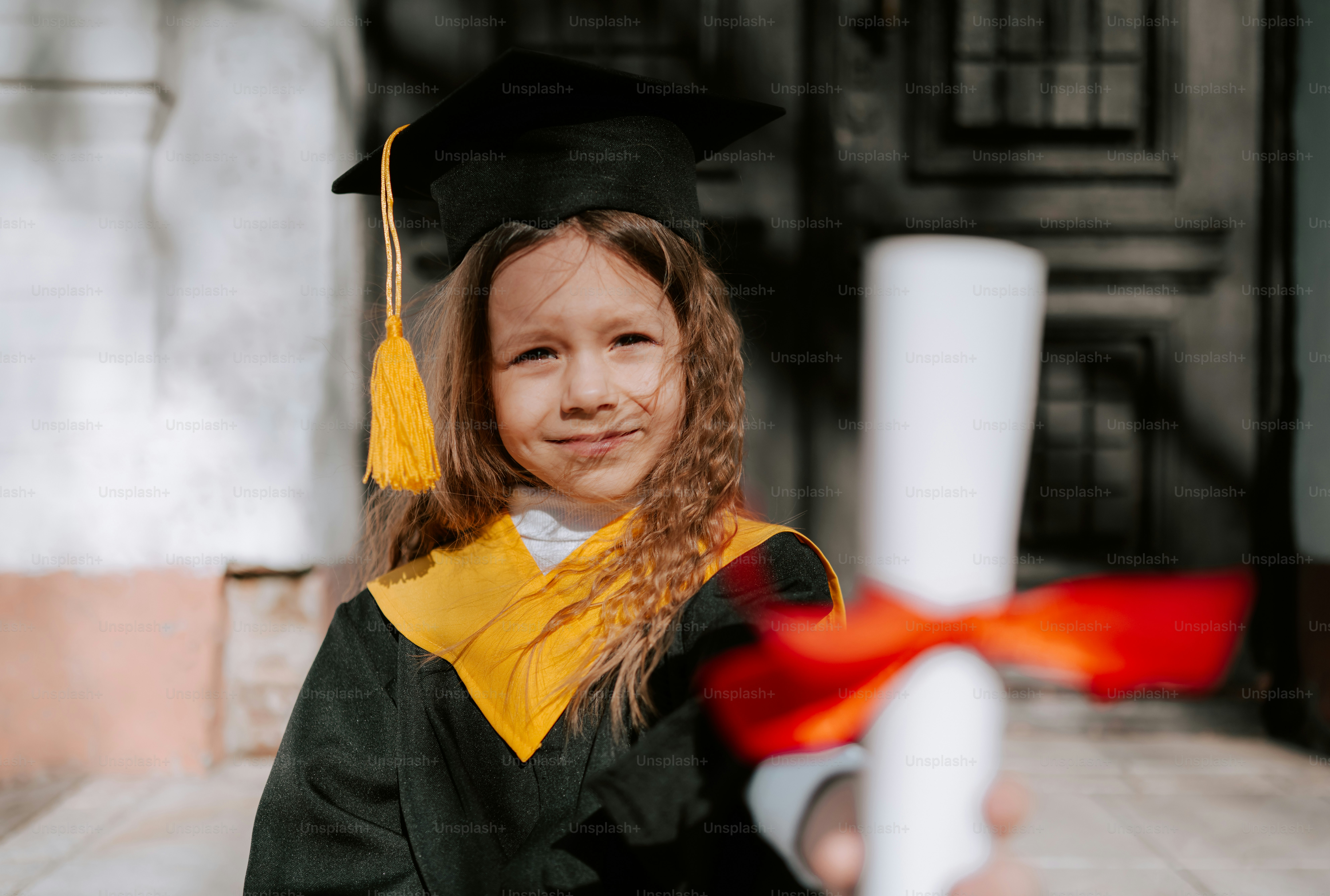 A young graduate holds a diploma with a red ribbon.