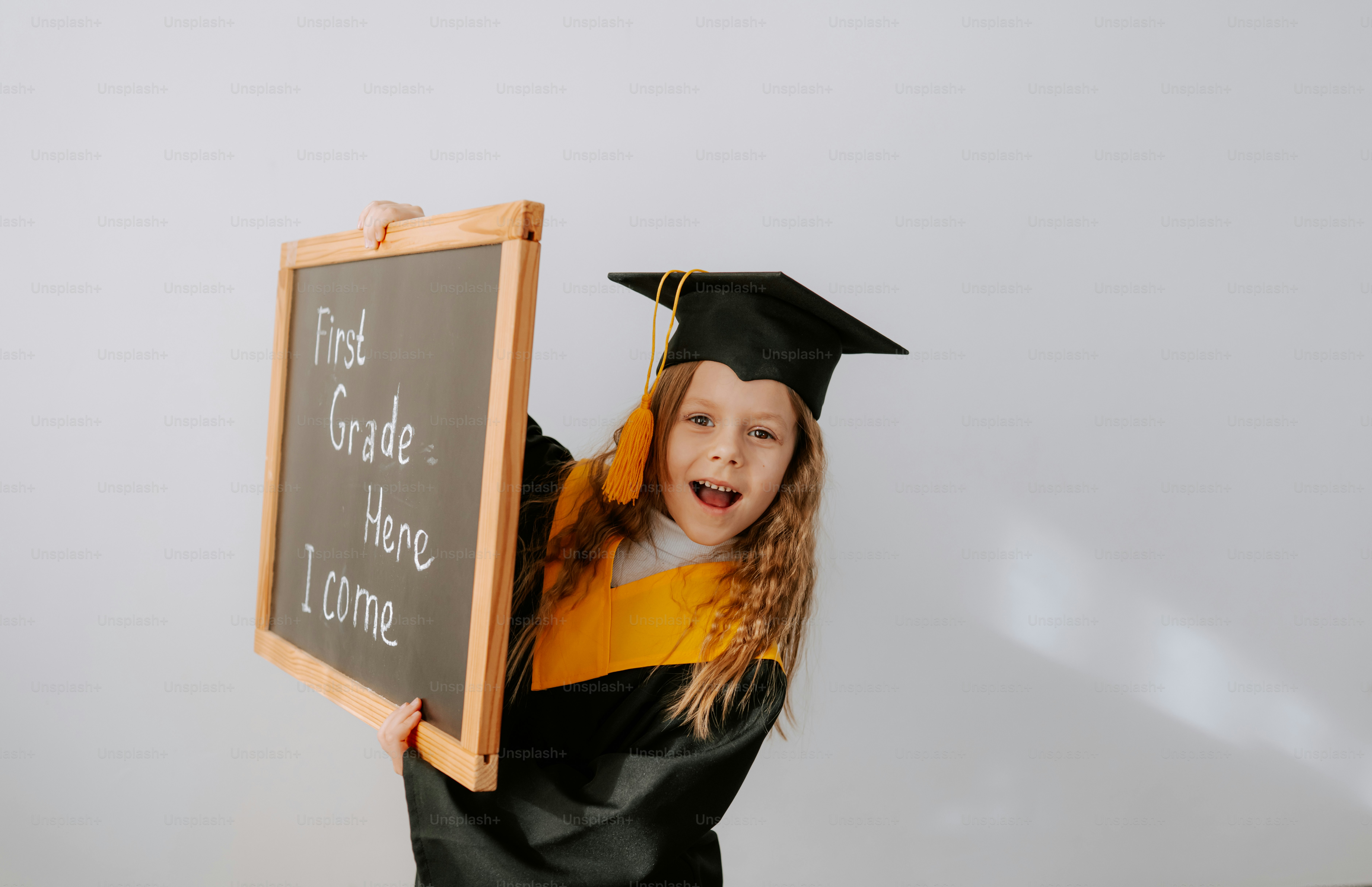 Girl in graduation cap holds a sign saying first grade