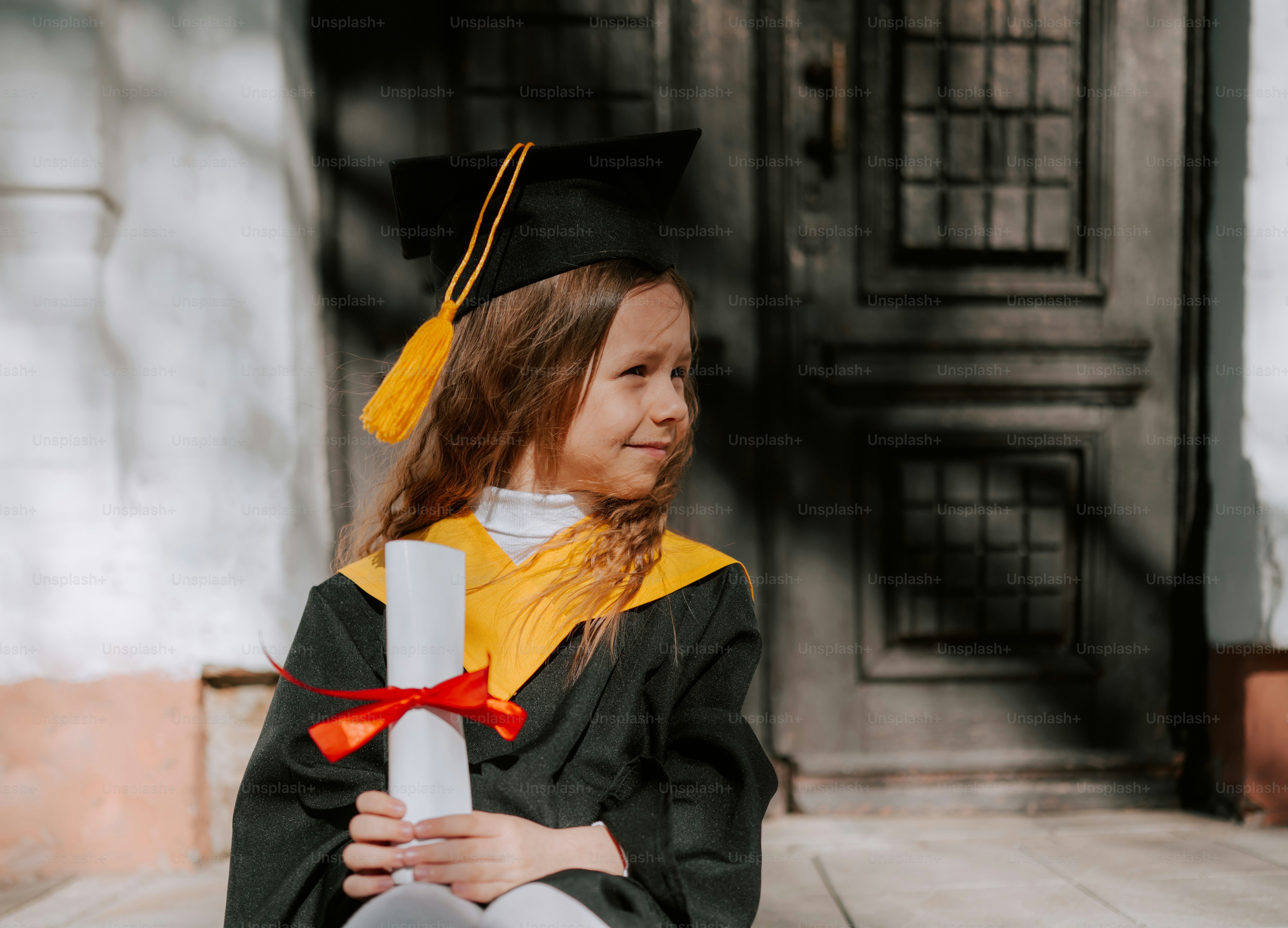 A young girl in graduation attire holds a diploma.