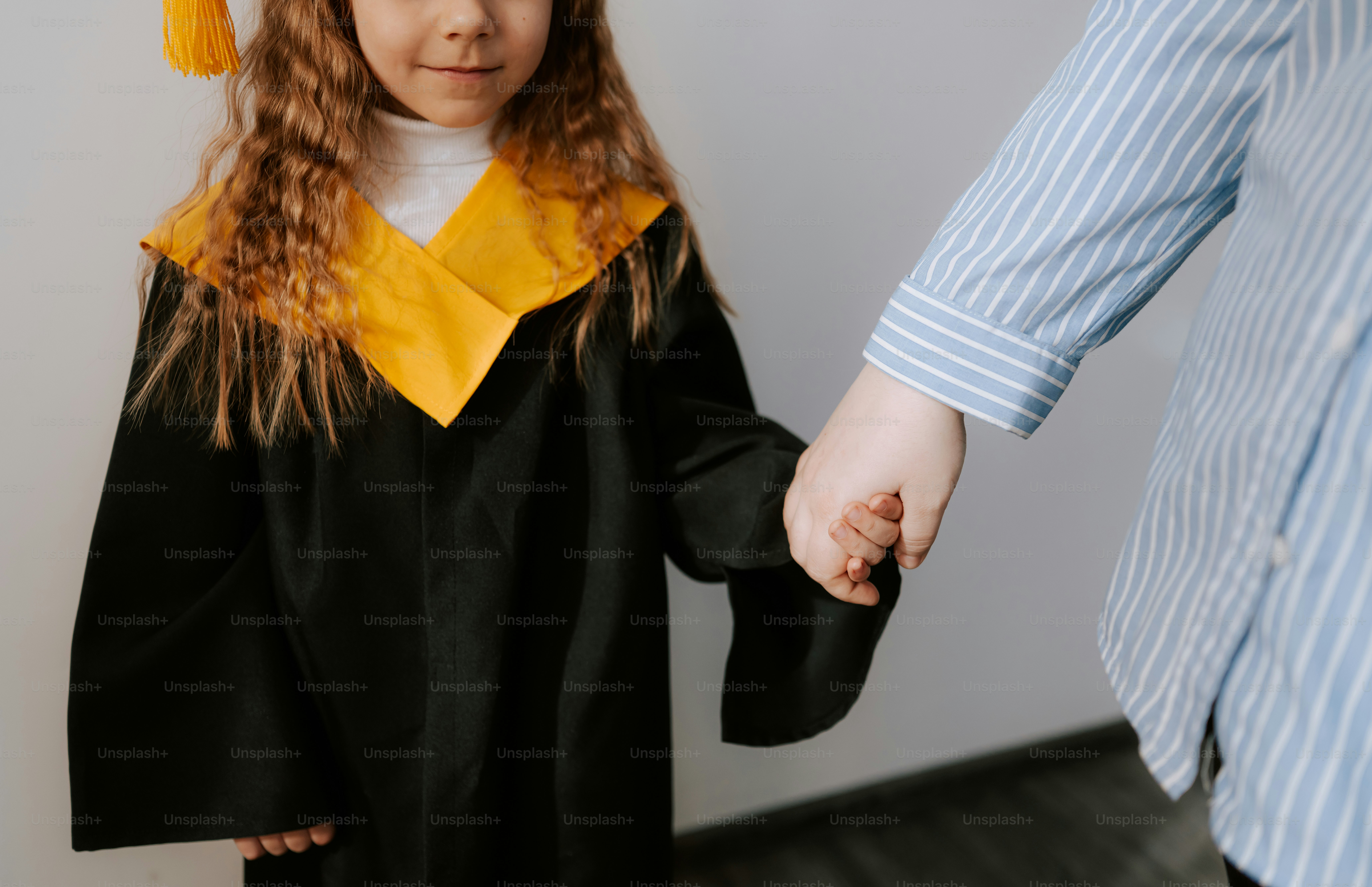 A child in a graduation gown holds an adult's hand. photo – Education ...