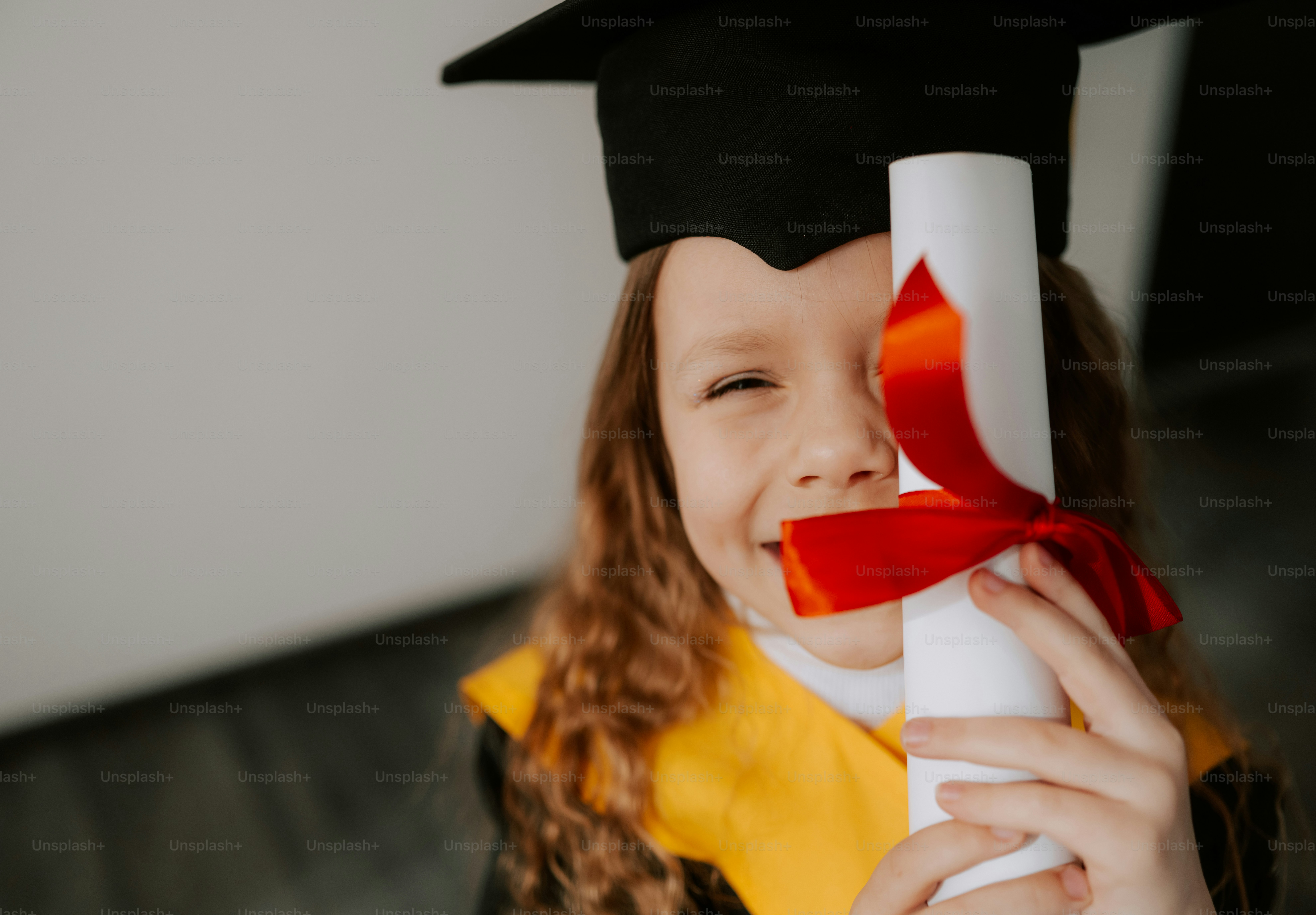 A smiling child in graduation cap holding a diploma