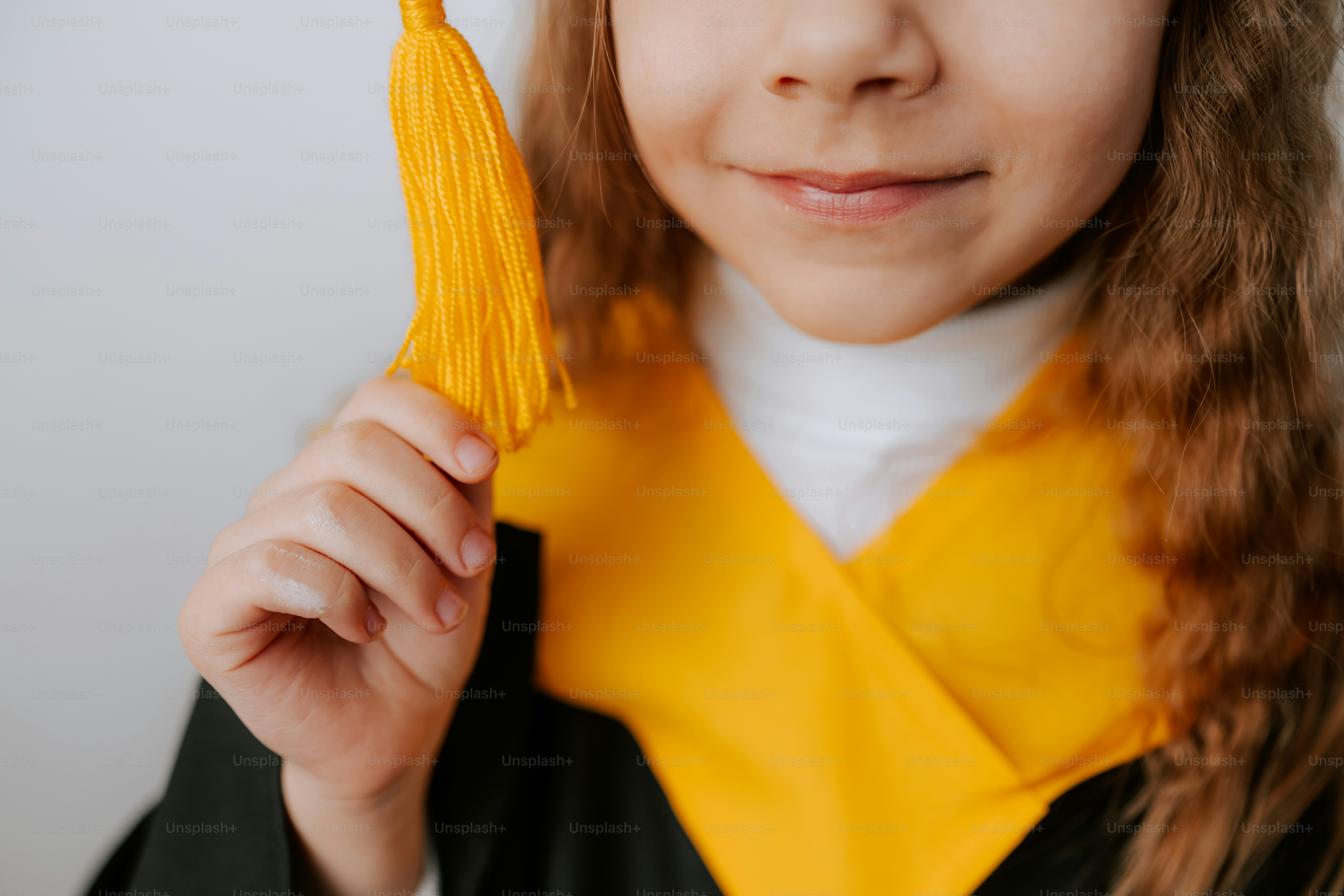 A young girl in graduation attire holds a tassel